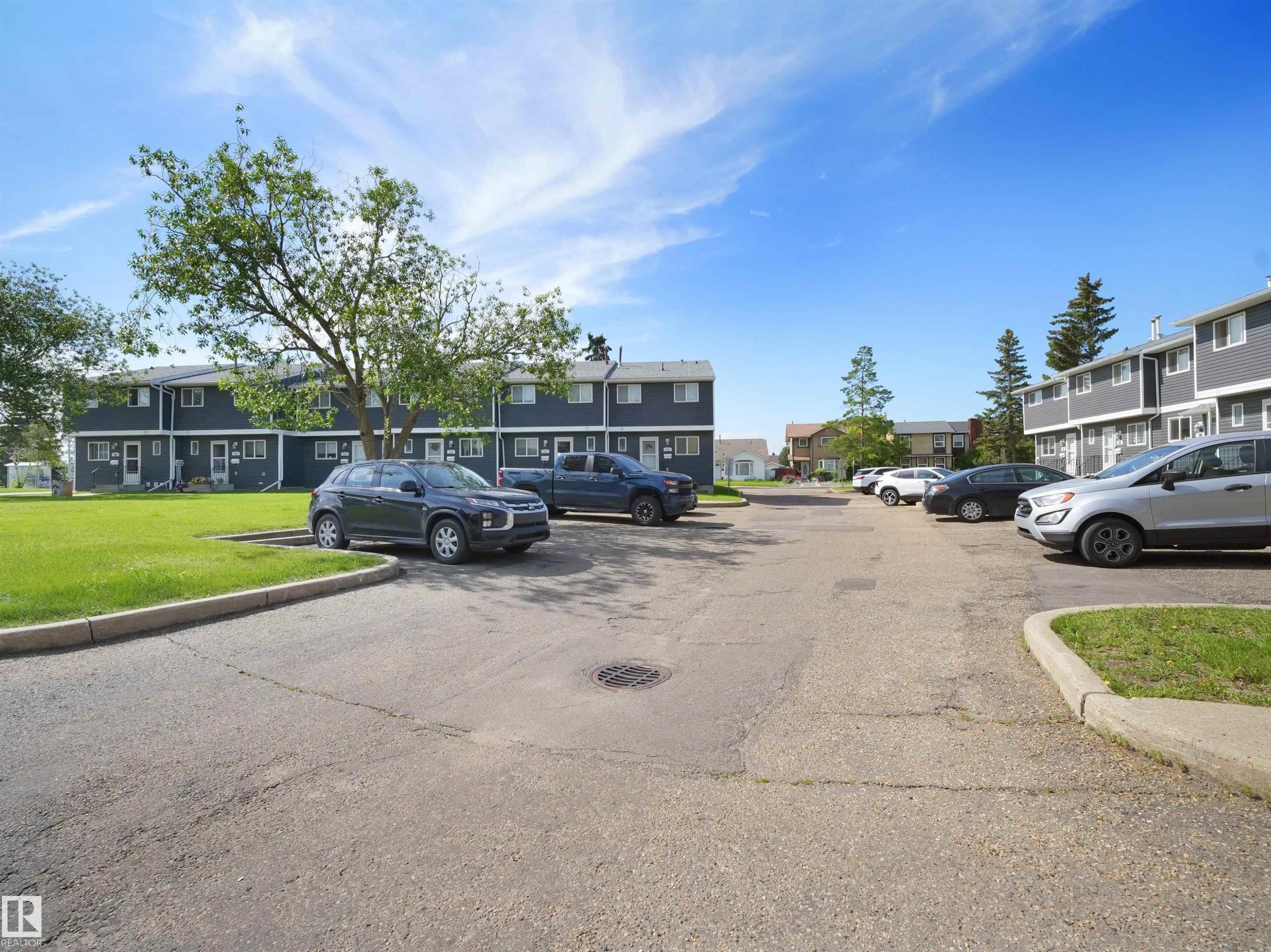 Paved parking area with concrete curbing, bordered by grassy sections and mature trees - 575 Dunluce Road, Edmonton, AB