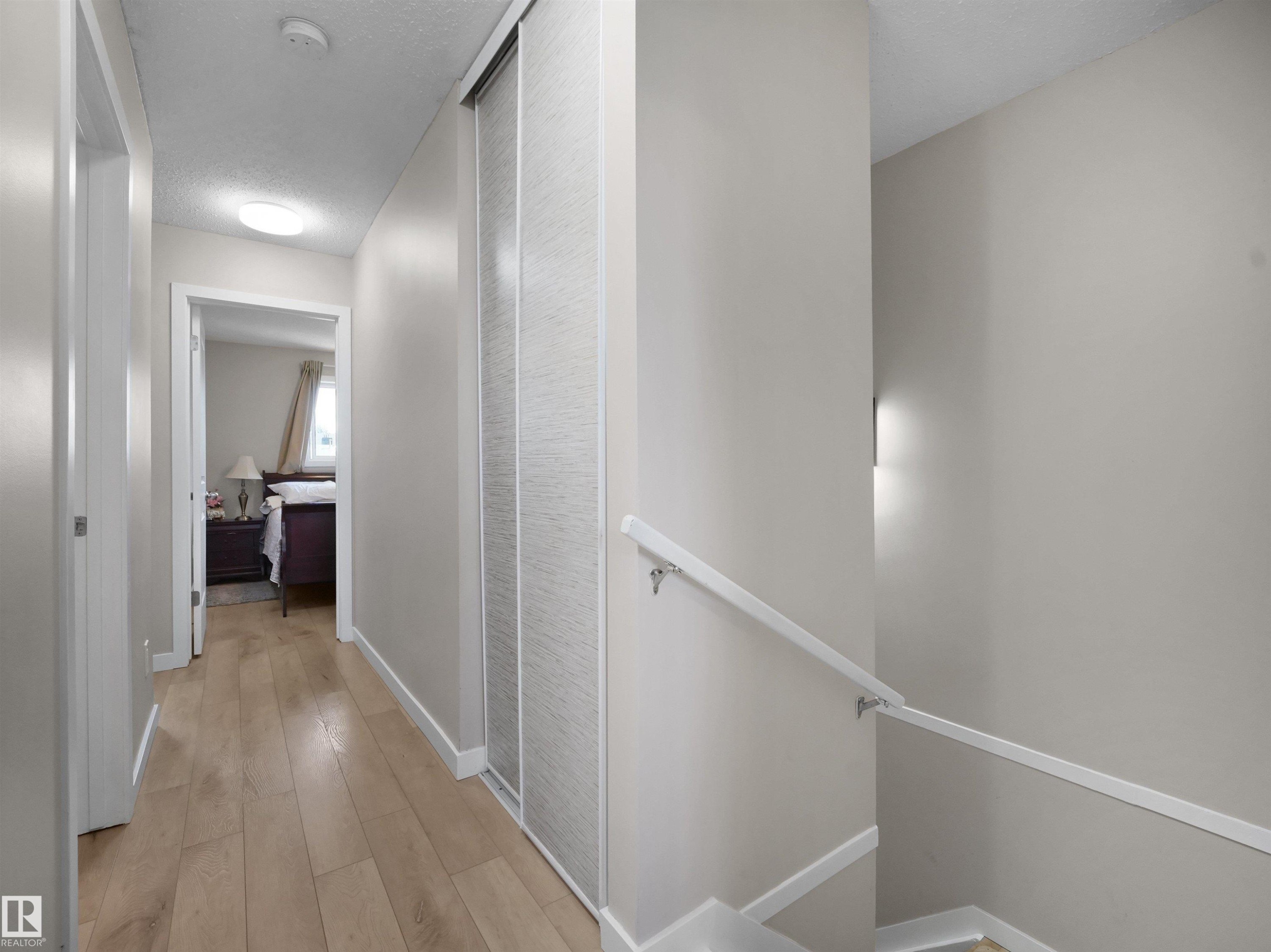 Hallway featuring wood-finish flooring, light neutral paint, and white trim - 575 Dunluce Road, Edmonton, AB