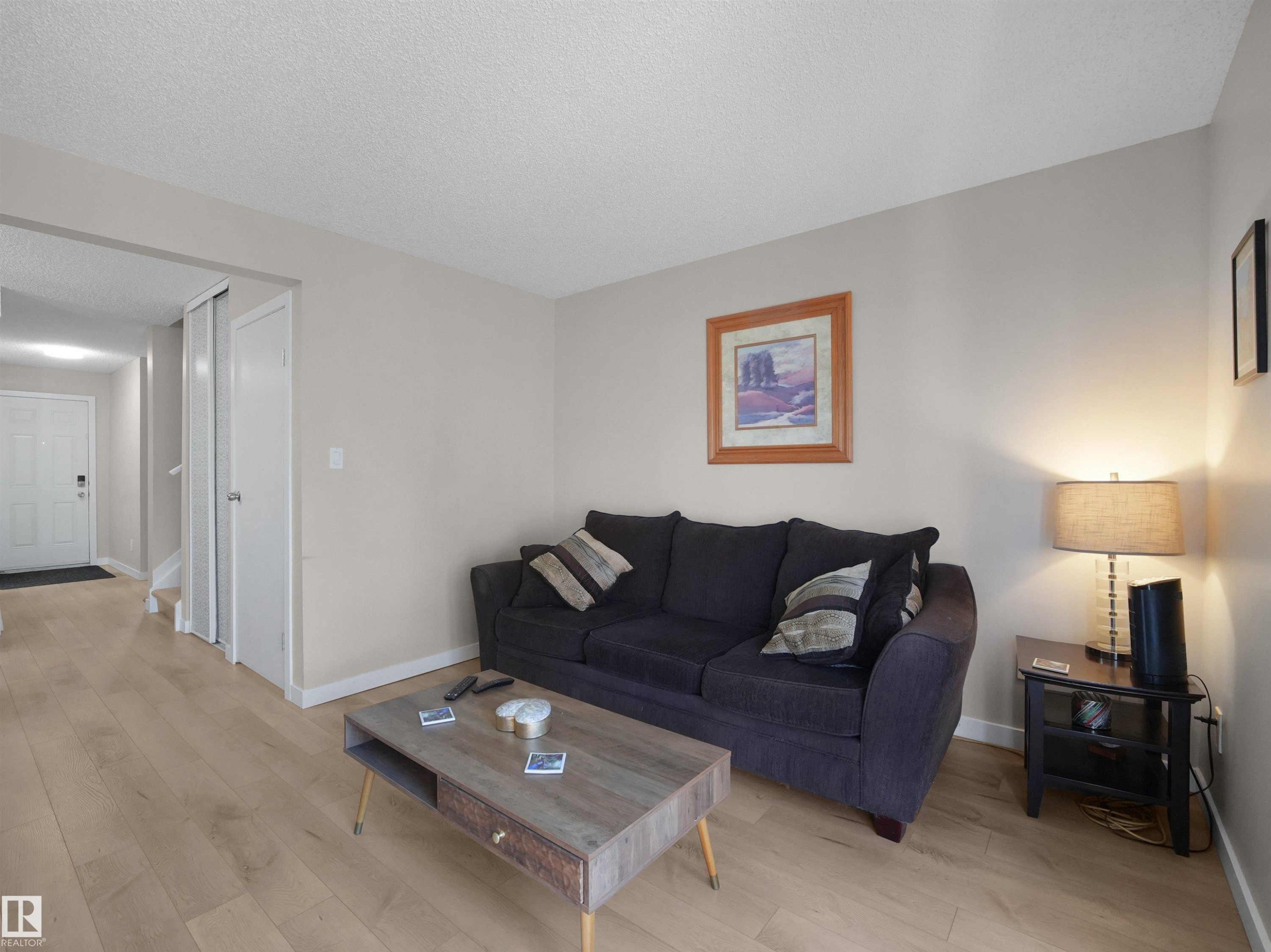 Living area featuring light wood-finish flooring, neutral wall tones, white baseboards, and a white entry door - 575 Dunluce Road, Edmonton, AB
