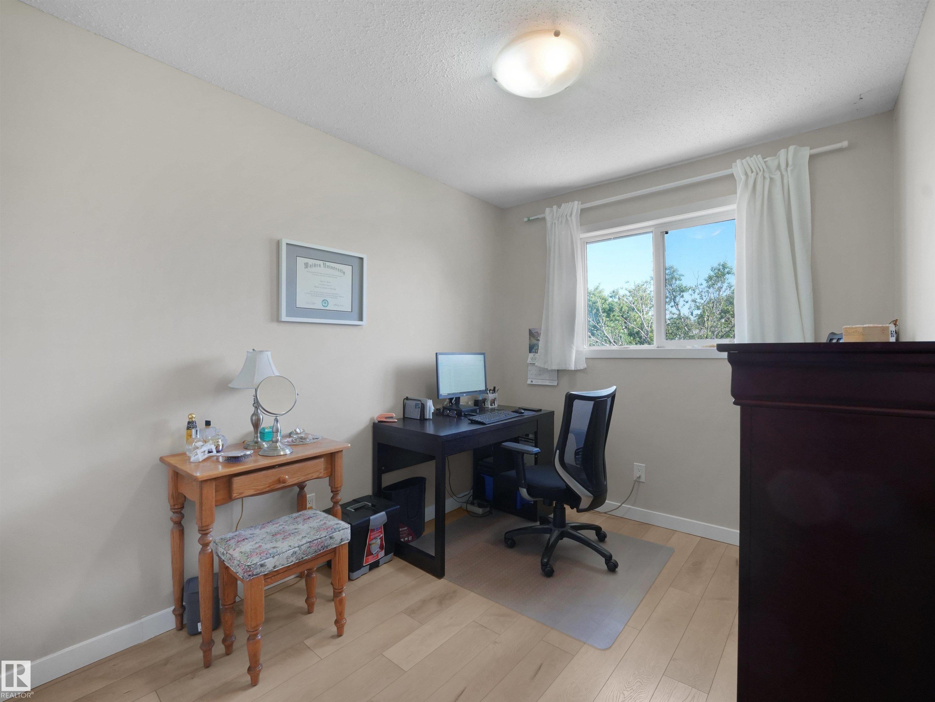 Room featuring light wood-finish flooring, neutral wall tones, and a window with white curtains - 575 Dunluce Road, Edmonton, AB