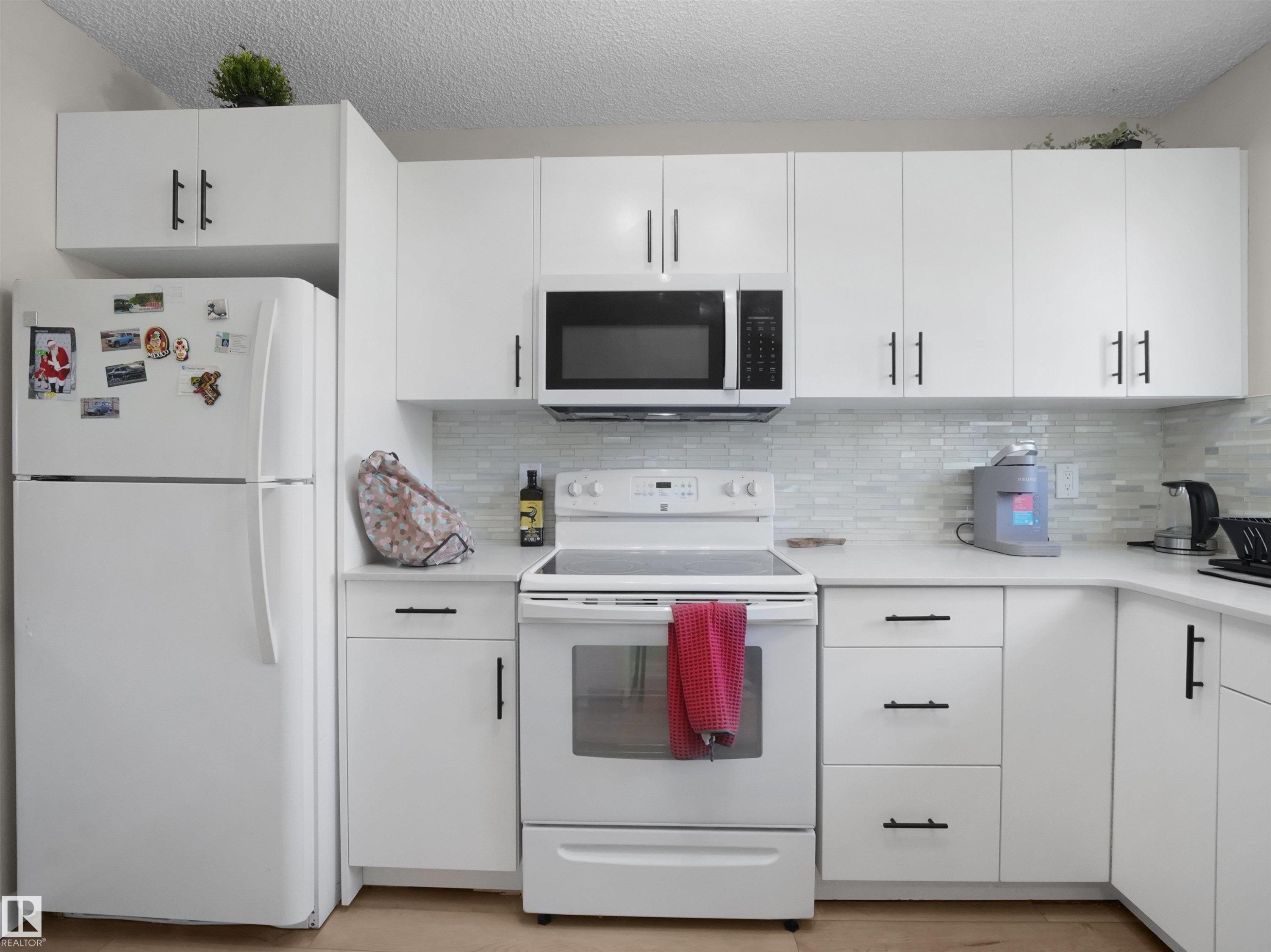 Contemporary kitchen featuring white cabinetry, black hardware, white countertops, and a white tile backsplash - 575 Dunluce Road, Edmonton, AB