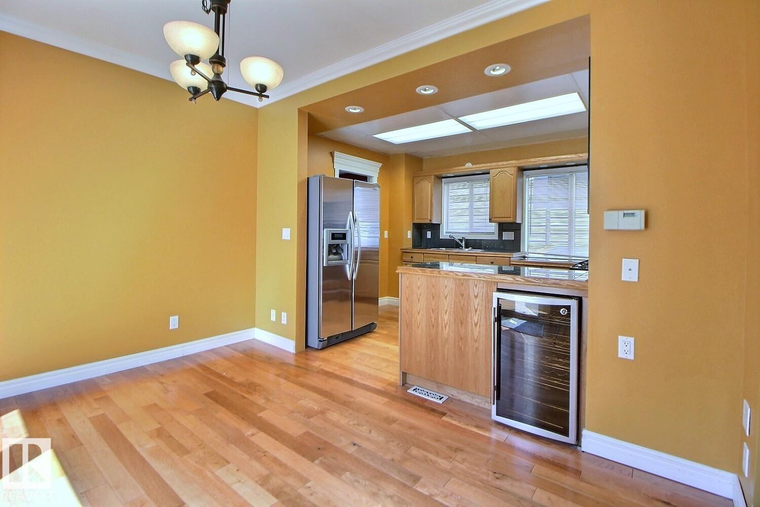 Dining area featuring wood-finish flooring, a contemporary chandelier, and crown molding - 11312 127 Street Nw, Edmonton, AB
