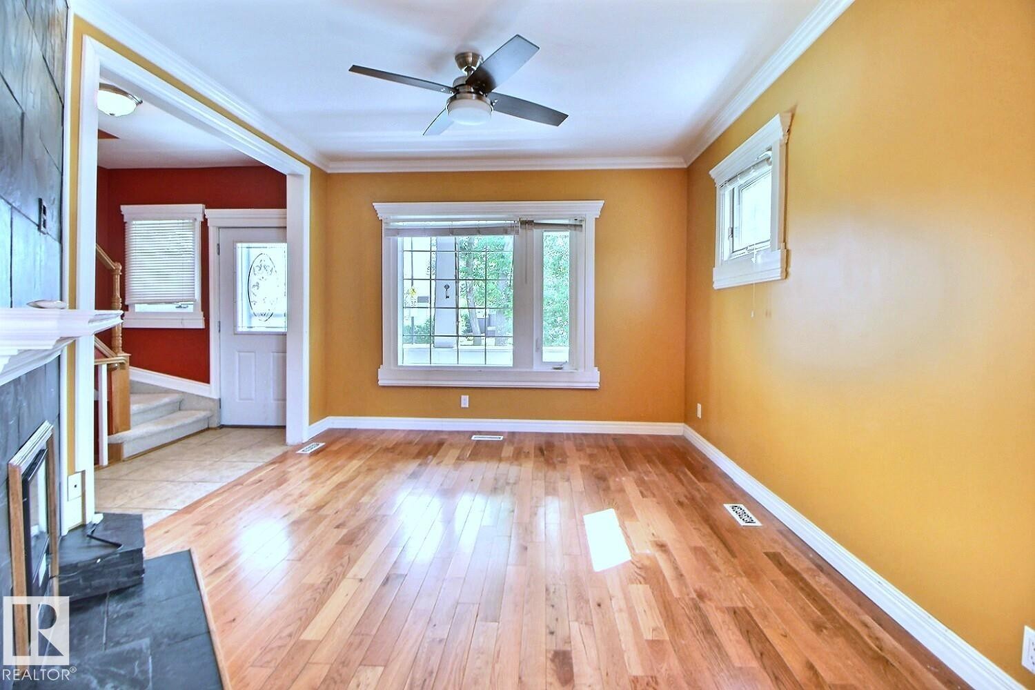 Living area featuring light wood-finish flooring, a ceiling fan with integrated lighting, and multiple windows with white trim - 11312 127 Street Nw, Edmonton, AB