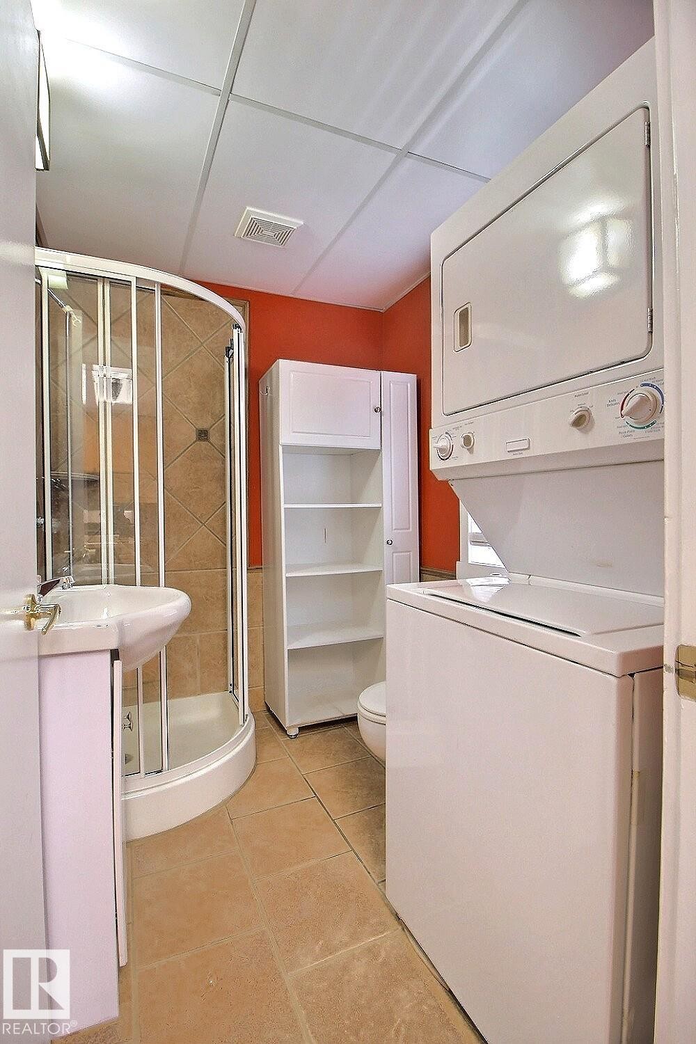 Compact bathroom featuring a corner shower, pedestal sink, and stackable laundry appliances - 11312 127 Street Nw, Edmonton, AB