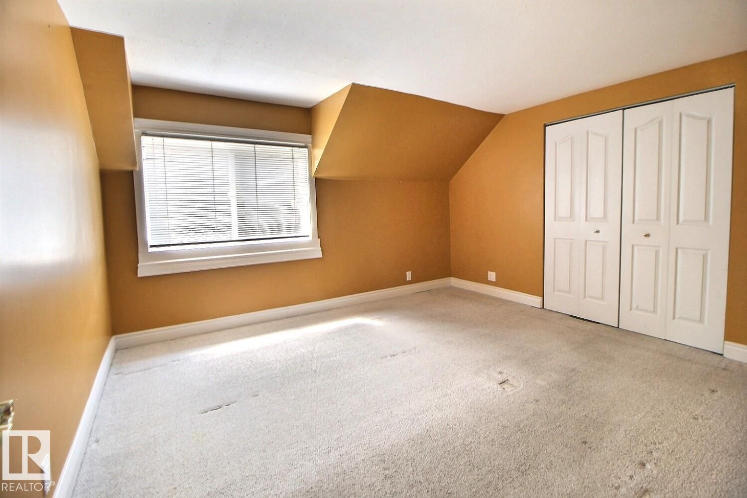 Room featuring sloped ceilings, a single window with white trim, and a pair of bi-fold closet doors - 11312 127 Street Nw, Edmonton, AB