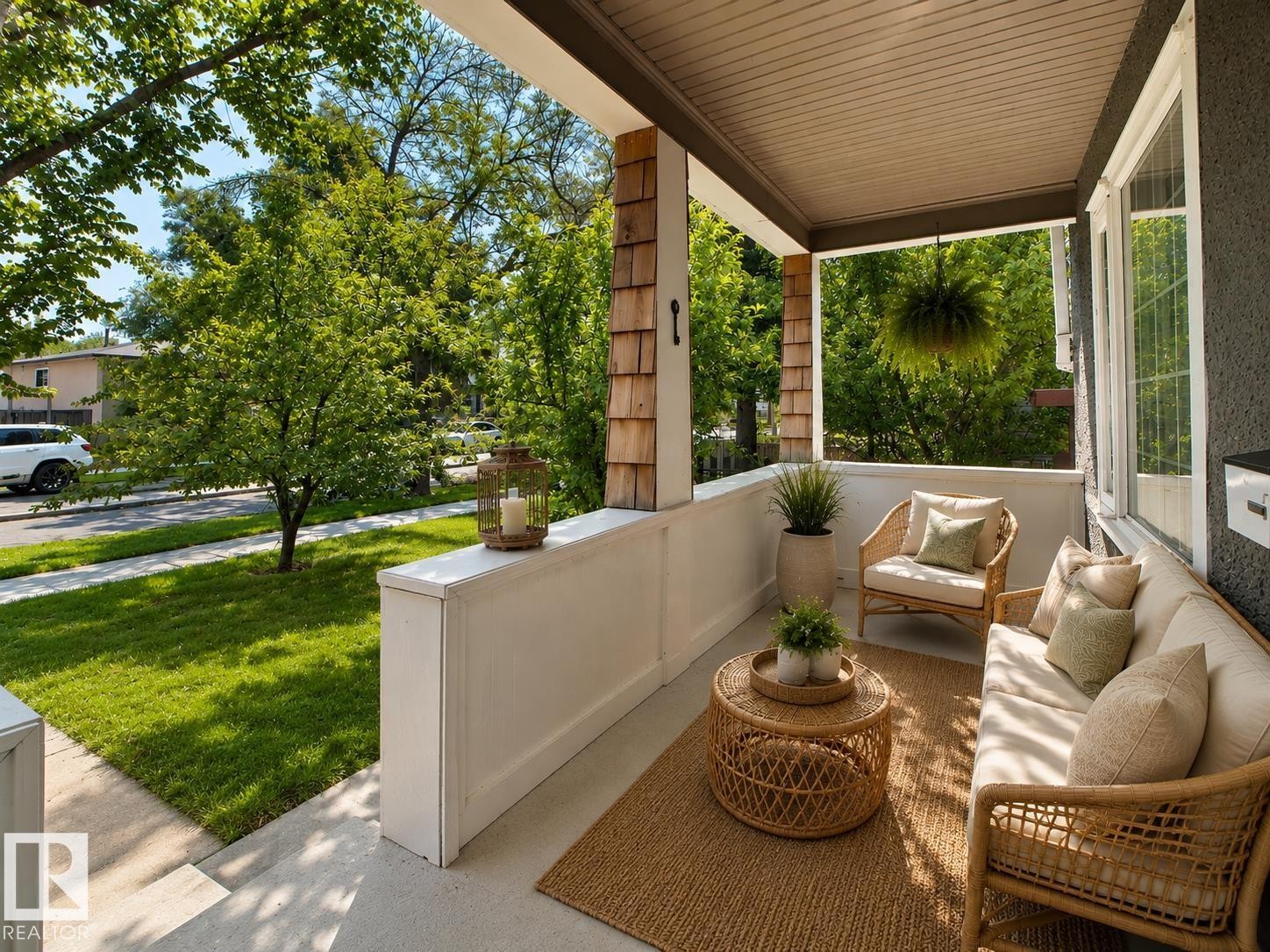 Covered front porch featuring a textured ceiling, a cedar shingle accent wall, and painted white columns - 11312 127 Street Nw, Edmonton, AB