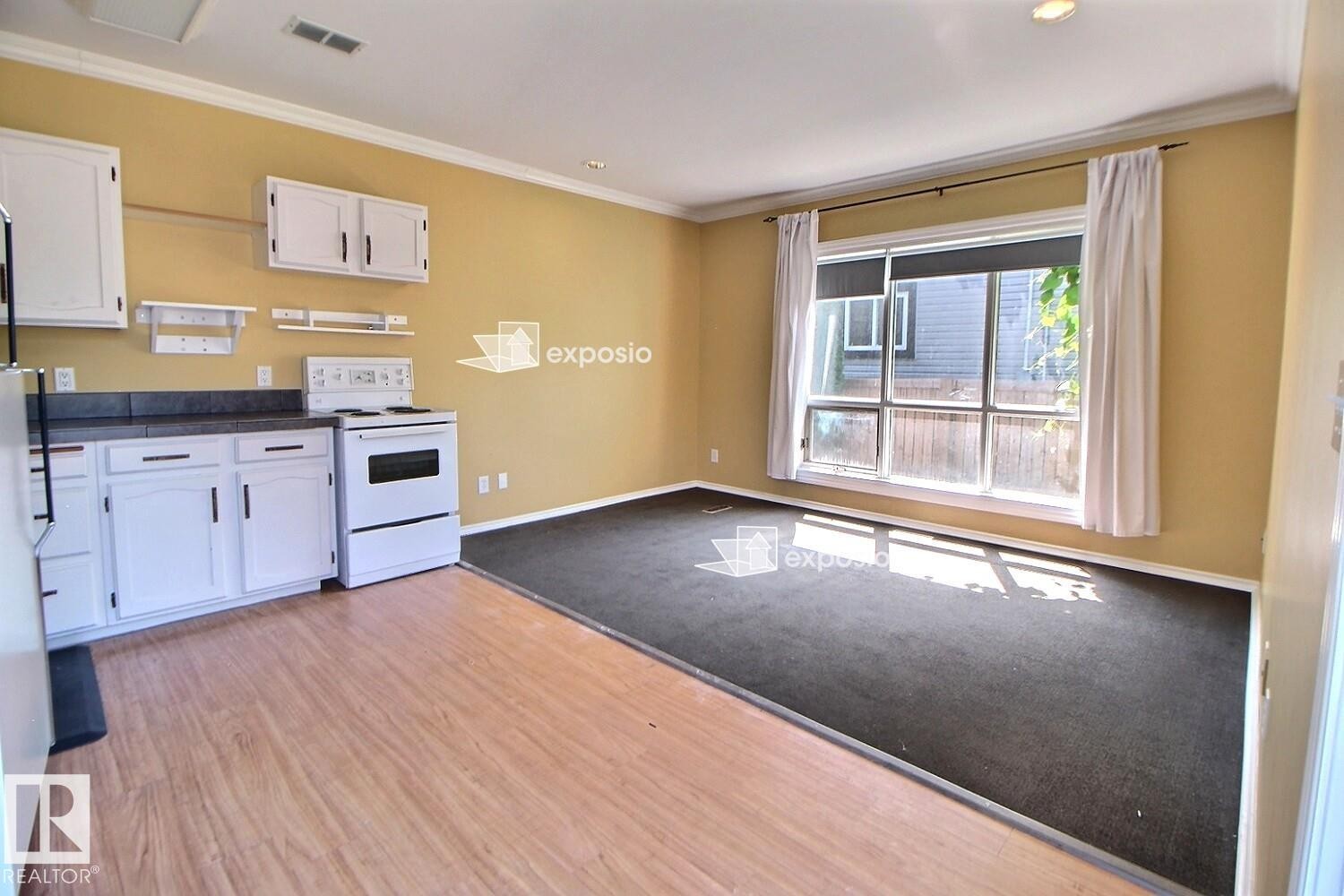 Kitchen area with wood-finish flooring, white cabinetry, and a built-in electric range - 11312 127 Street Nw, Edmonton, AB