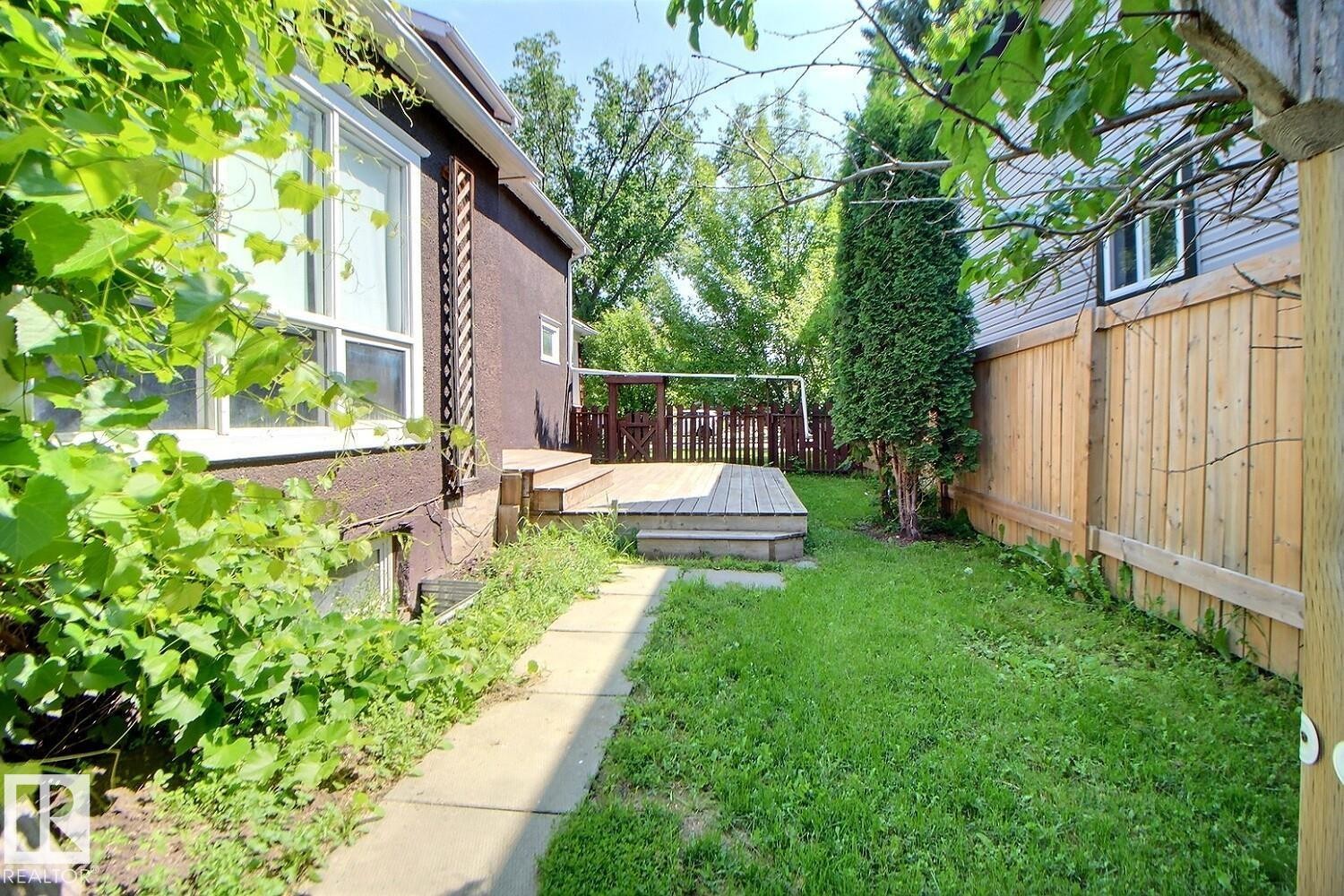 Expansive outdoor deck with wood railings, overlooking a grassy yard with a concrete pathway - 11312 127 Street Nw, Edmonton, AB