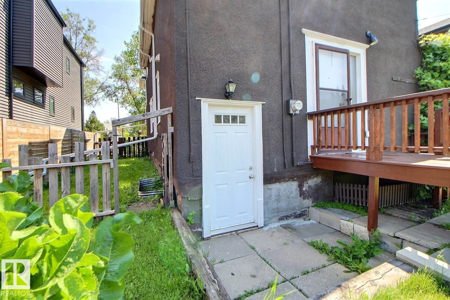 Exterior stucco finish featuring a white door with transom-style lites and an adjacent wood deck with a railing - 11312 127 Street Nw, Edmonton, AB