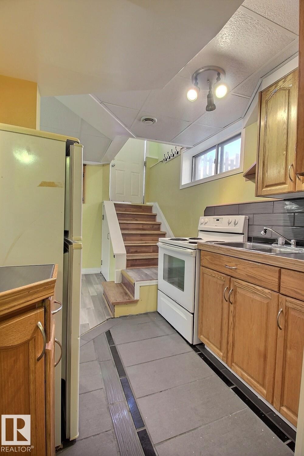 Kitchen area featuring wood-finish cabinetry, a ceramic tile backsplash, and a built-in sink - 11312 127 Street Nw, Edmonton, AB