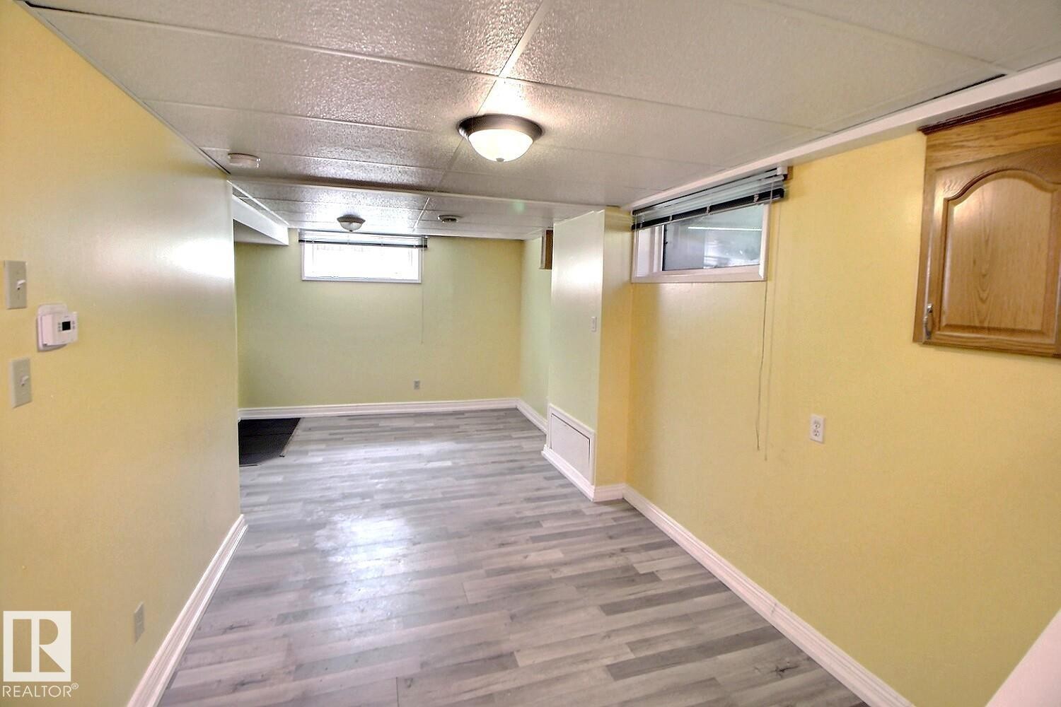 Finished lower level featuring light wood-finish flooring, drop ceiling with recessed lighting, and a wall-mounted wooden cabinet - 11312 127 Street Nw, Edmonton, AB