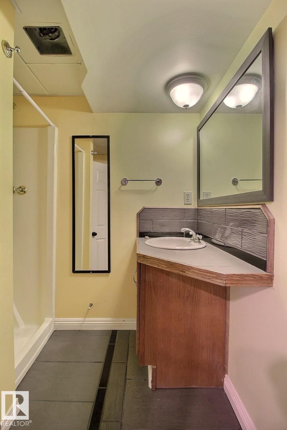 Bathroom featuring a wood-finish vanity with an integrated sink, a large framed mirror, and a tile backsplash - 11312 127 Street Nw, Edmonton, AB
