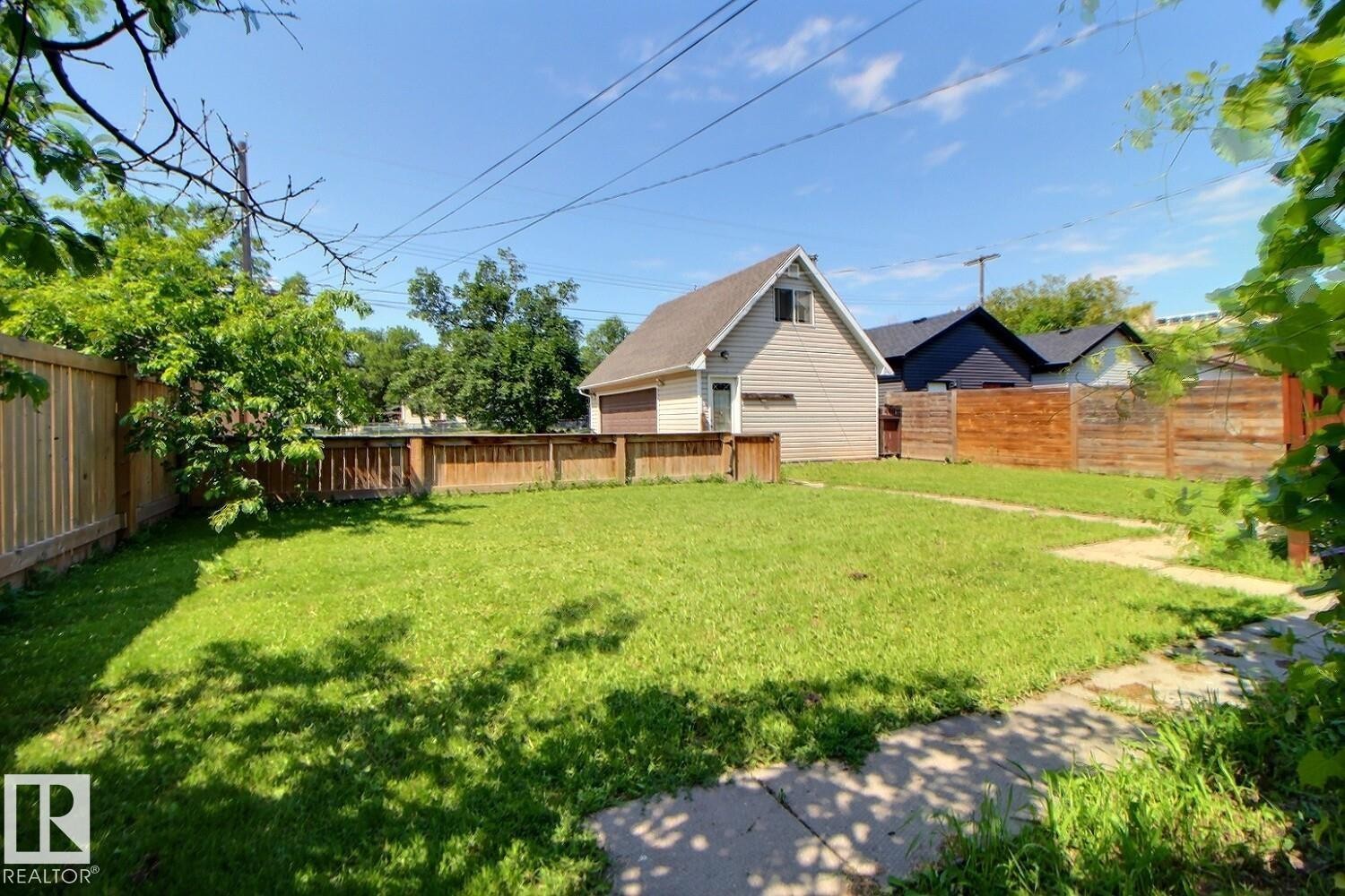 Expansive grassy yard area with a detached garage featuring light-colored siding and a brown garage door - 11312 127 Street Nw, Edmonton, AB