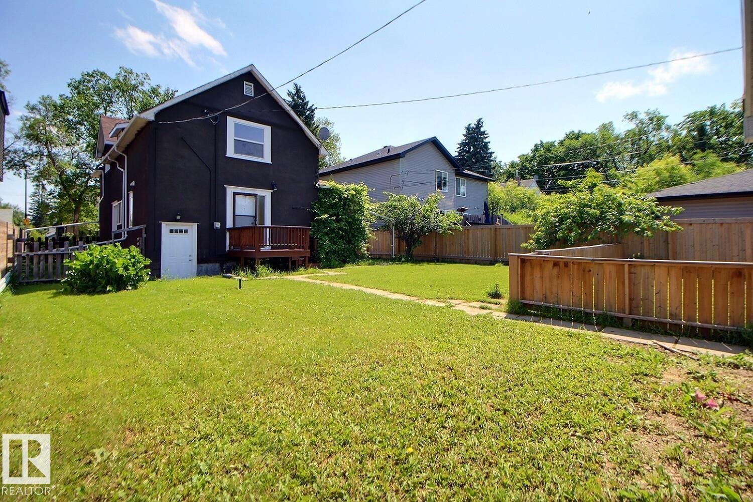 Expansive rear yard featuring a large grass area, wood privacy fencing, and a dark-toned residence with white trim - 11312 127 Street Nw, Edmonton, AB