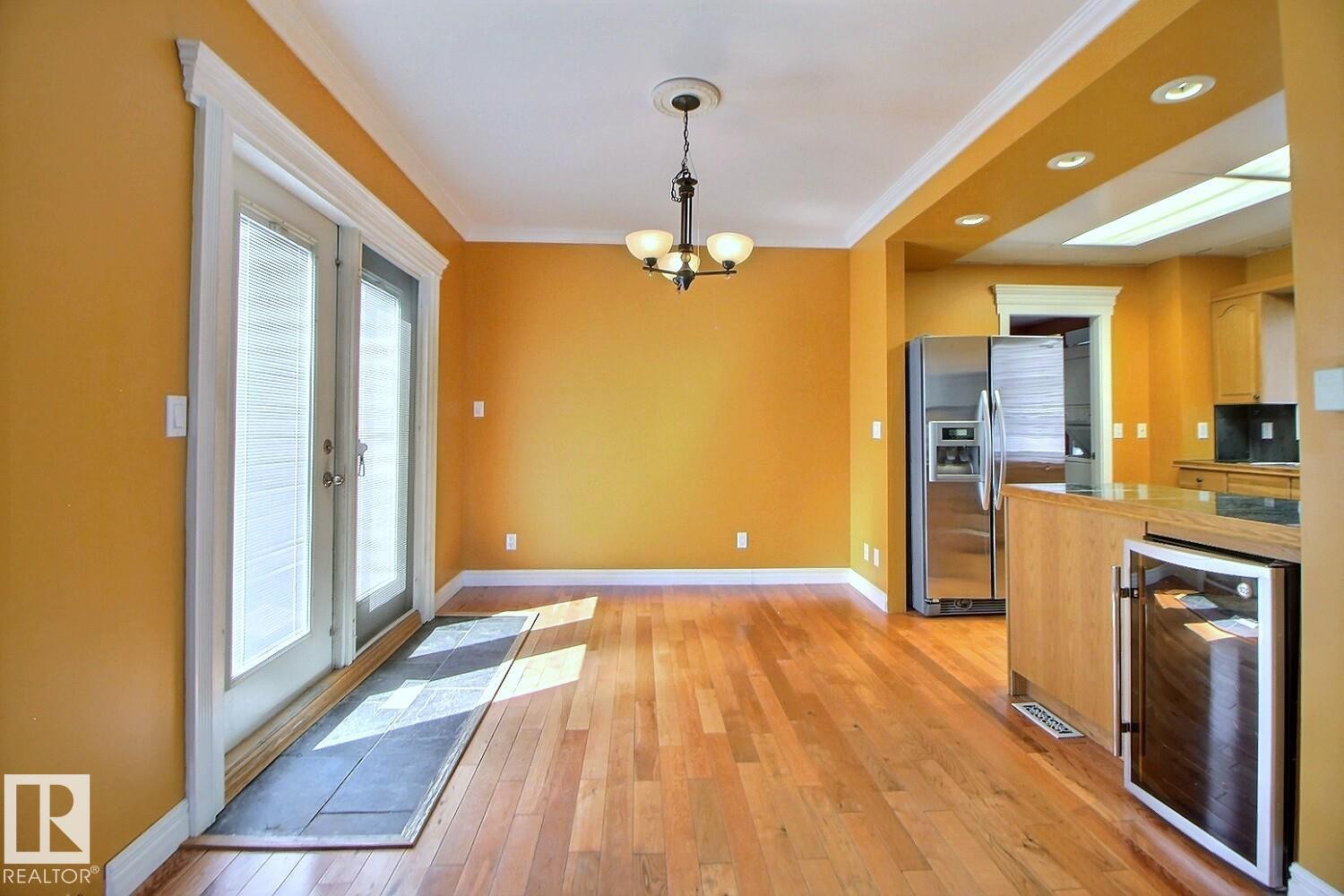 Hardwood flooring spans this open-concept room, featuring double glass-paneled doors with internal blinds - 11312 127 Street Nw, Edmonton, AB