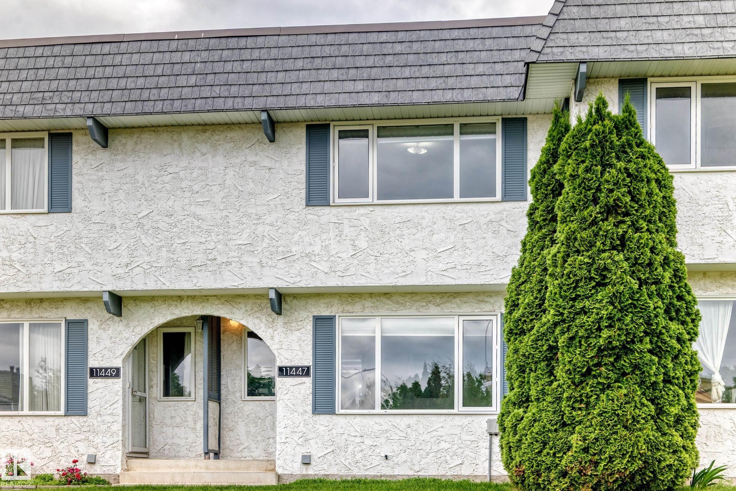 Multi-story exterior with textured stucco finish, dark gray shingle roofing, and blue decorative shutters - 11447 22 Avenue Nw, Edmonton, AB - Outdoor With Exterior