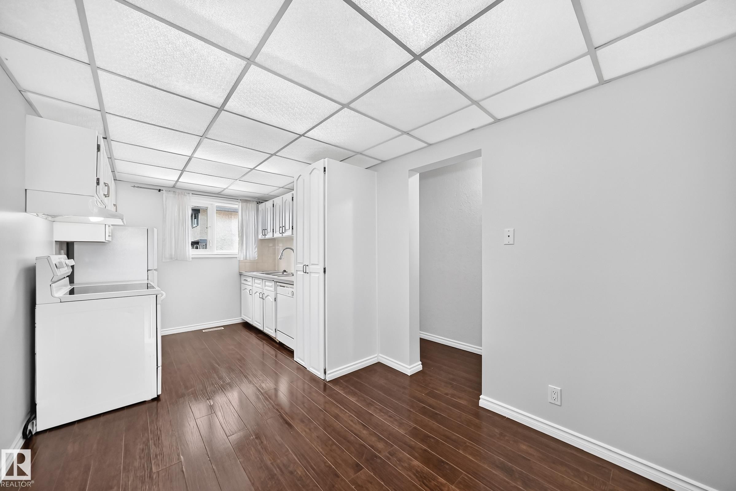 Open-concept kitchen area featuring wood-finish flooring, white cabinetry, and a drop ceiling with grid lighting - 11447 22 Avenue Nw, Edmonton, AB - Indoor