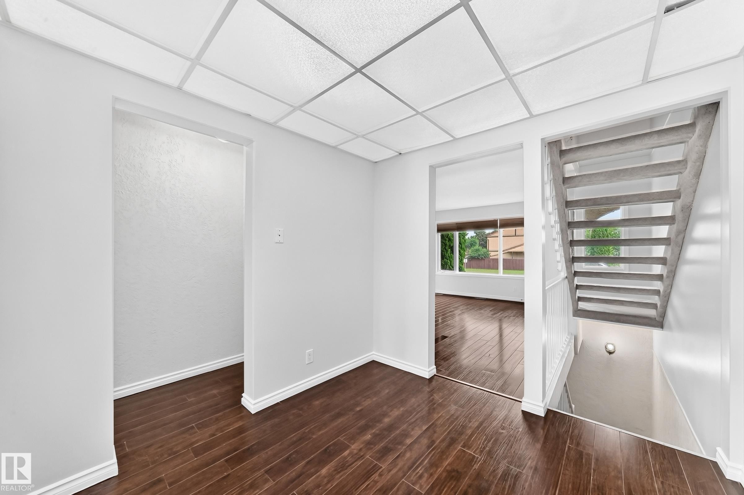 Hardwood-finish flooring extends through multiple rooms and features white baseboards, offering a cohesive aesthetic - 11447 22 Avenue Nw, Edmonton, AB - Indoor Photo Showing Other Room