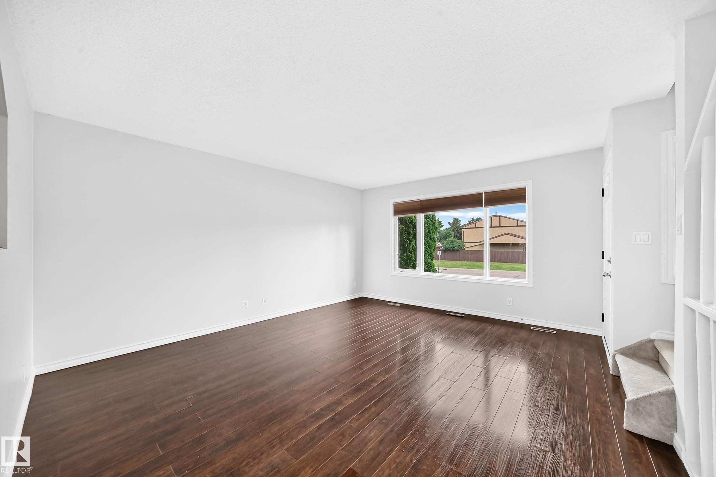 Spacious room with dark wood-finish flooring, white walls, and a large multi-pane window - 11447 22 Avenue Nw, Edmonton, AB - Indoor Photo Showing Other Room