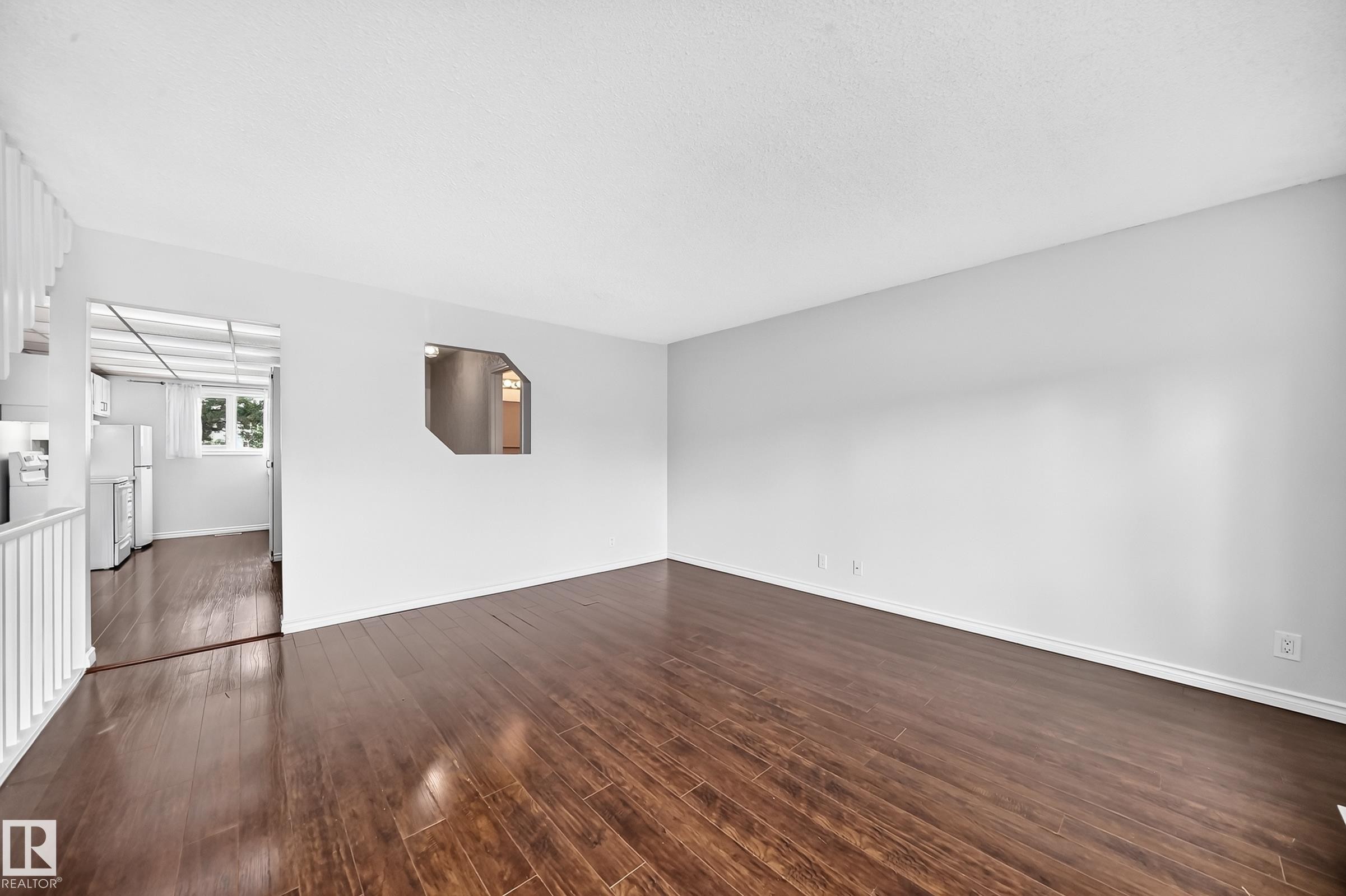 Spacious living area featuring wood-finish flooring, white wall paint, and a built-in architectural wall cut-out - 11447 22 Avenue Nw, Edmonton, AB - Indoor Photo Showing Other Room