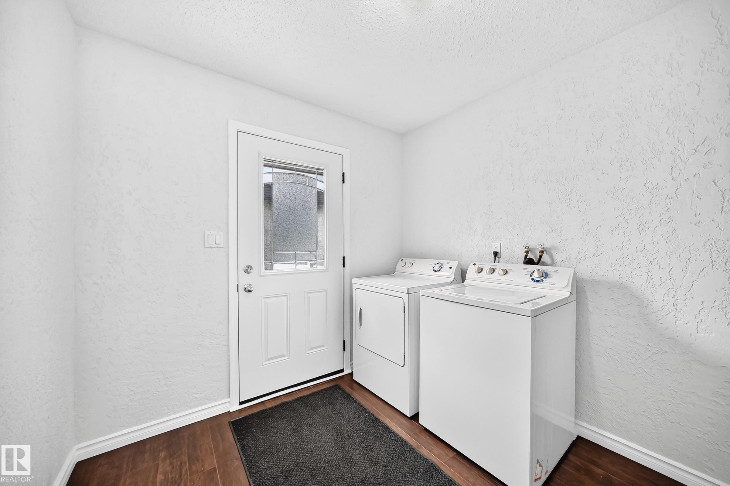 Dedicated laundry area featuring a white paneled door with an etched glass insert, wood-finish flooring, and white baseboards - 11447 22 Avenue Nw, Edmonton, AB - Indoor Photo Showing Laundry Room