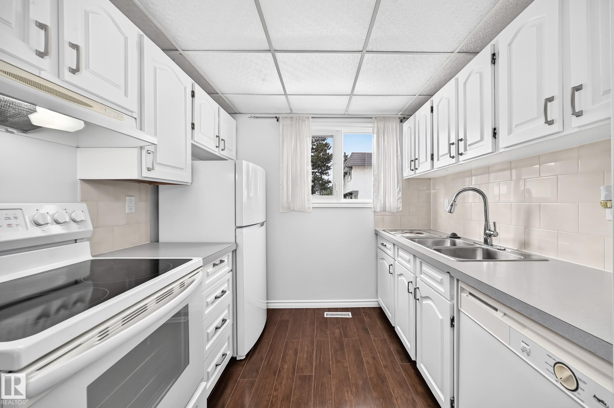 Galley-style kitchen featuring white cabinetry and dark wood-finish flooring - 11447 22 Avenue Nw, Edmonton, AB - Indoor Photo Showing Kitchen With Double Sink