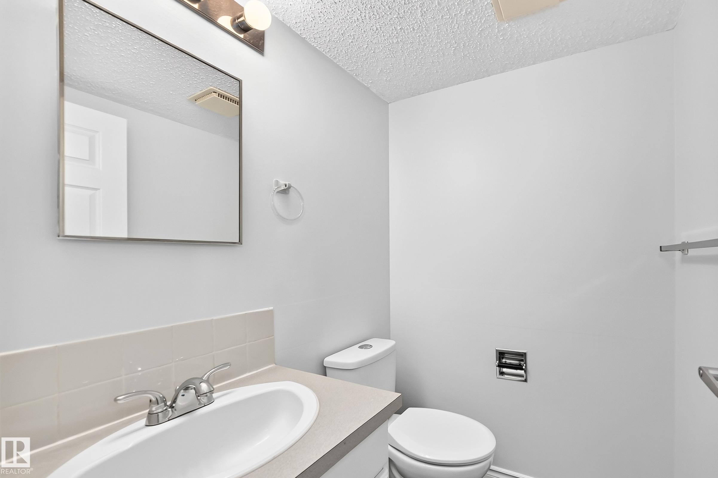 Bathroom featuring a vanity with an integrated sink, polished chrome faucet, and a wall-mounted mirror - 11447 22 Avenue Nw, Edmonton, AB - Indoor Photo Showing Bathroom