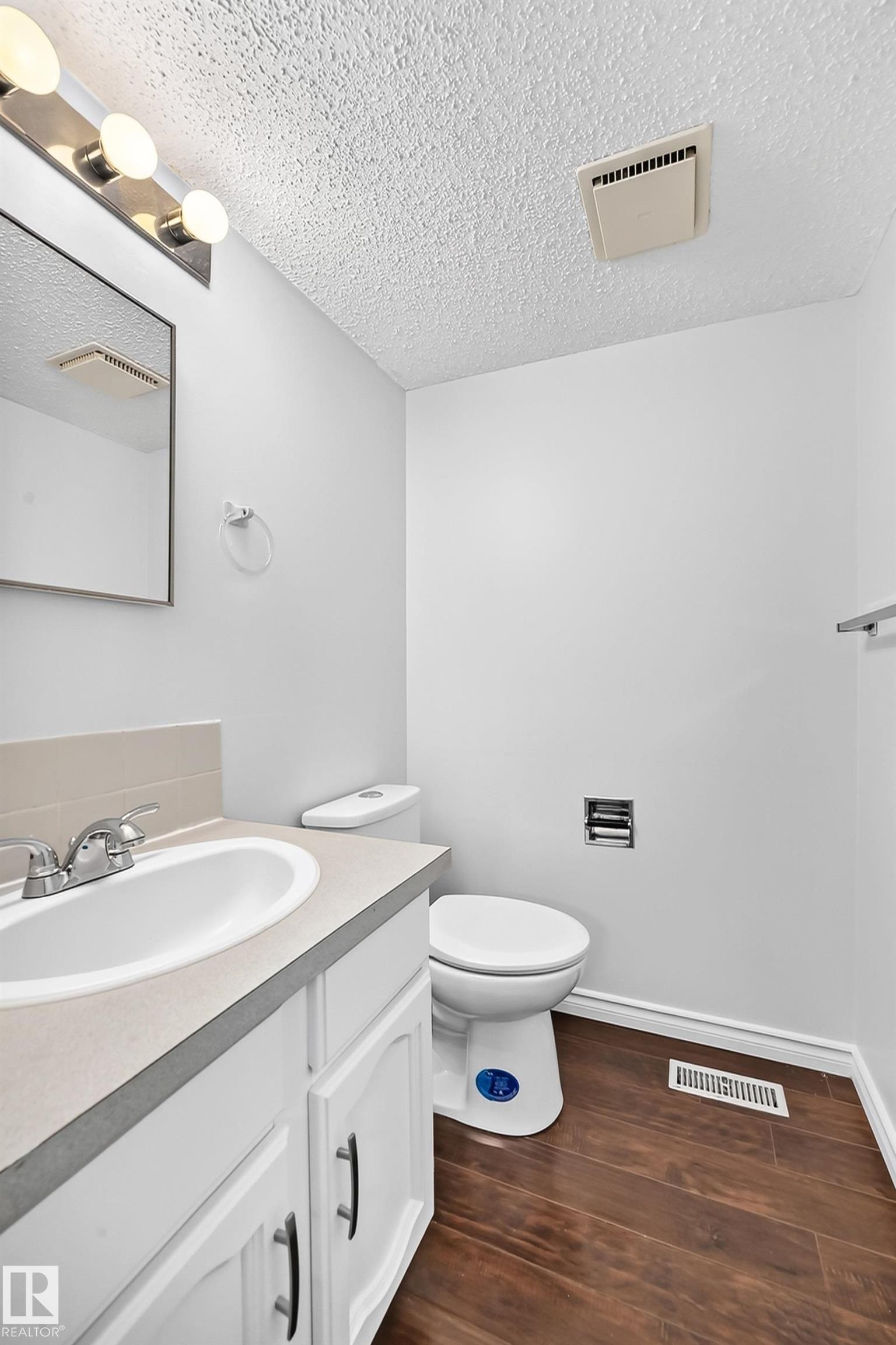 Bathroom featuring a white vanity with an integrated sink, chrome faucet, and dark wood-finish flooring - 11447 22 Avenue Nw, Edmonton, AB - Indoor Photo Showing Bathroom