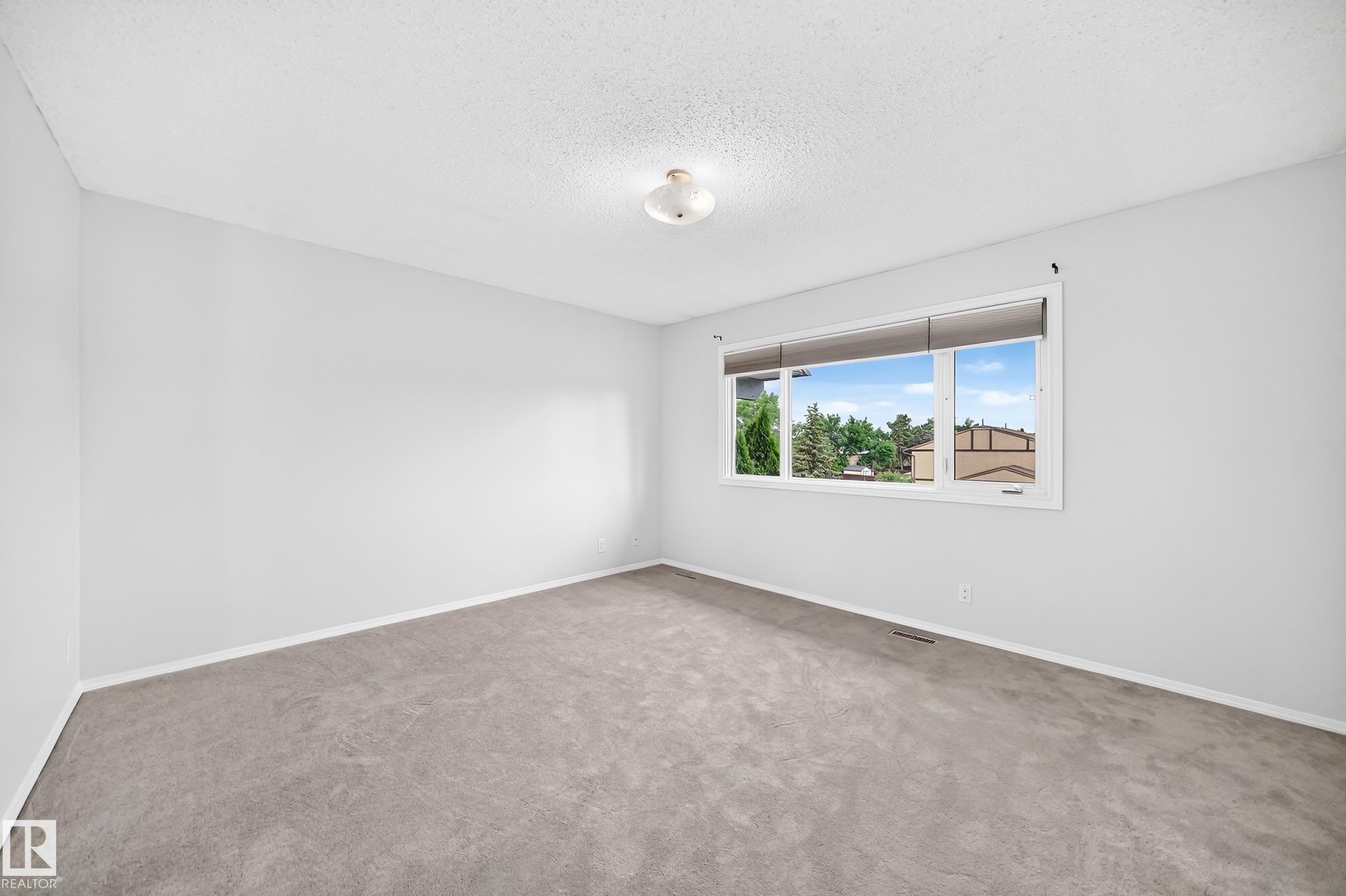 Spacious interior room featuring light gray carpeting, white walls, and a large window with white trim - 11447 22 Avenue Nw, Edmonton, AB - Indoor Photo Showing Other Room