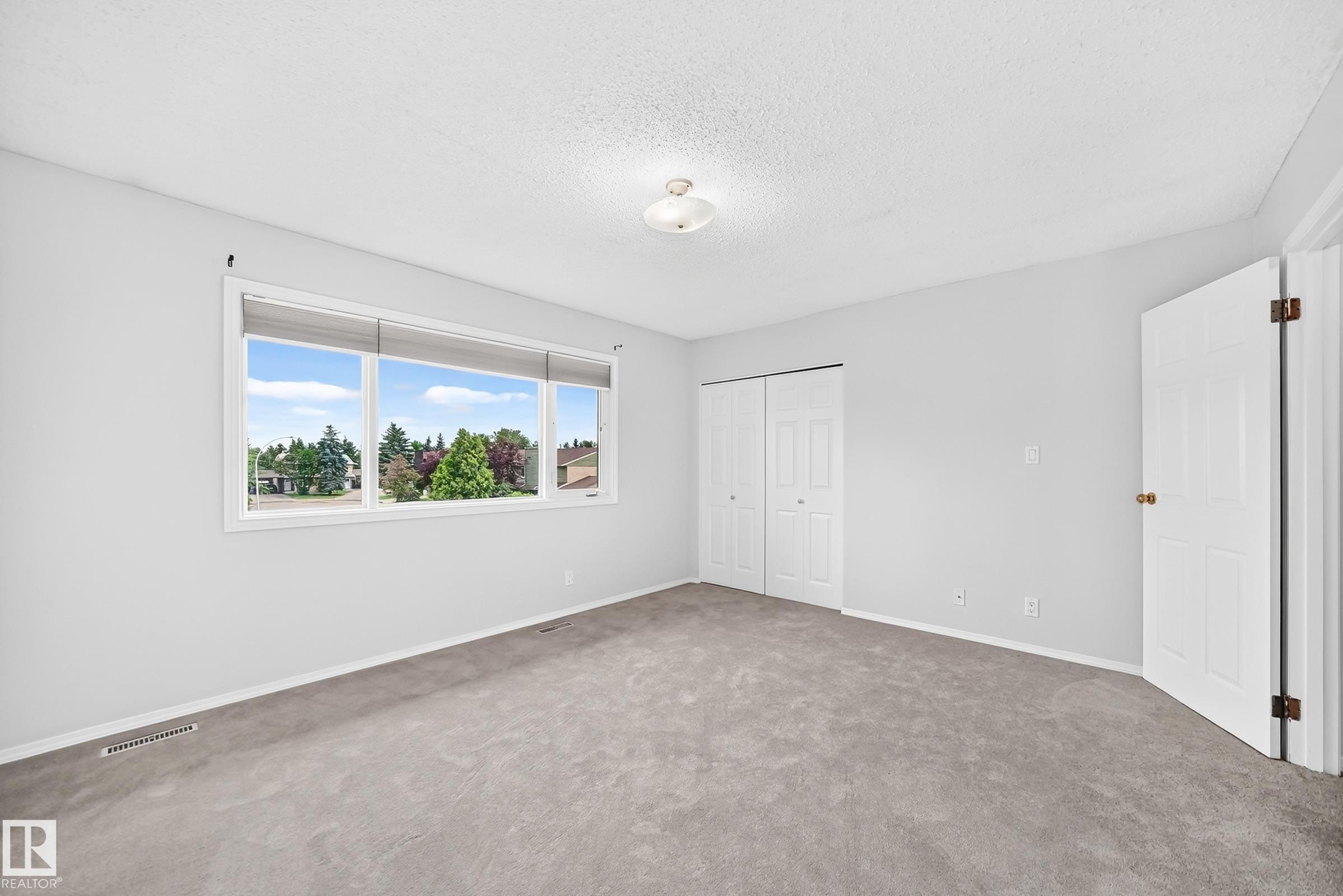 Spacious room featuring a large horizontal window, neutral gray carpeting, white walls, and a ceiling-mounted light fixture - 11447 22 Avenue Nw, Edmonton, AB - Indoor Photo Showing Other Room
