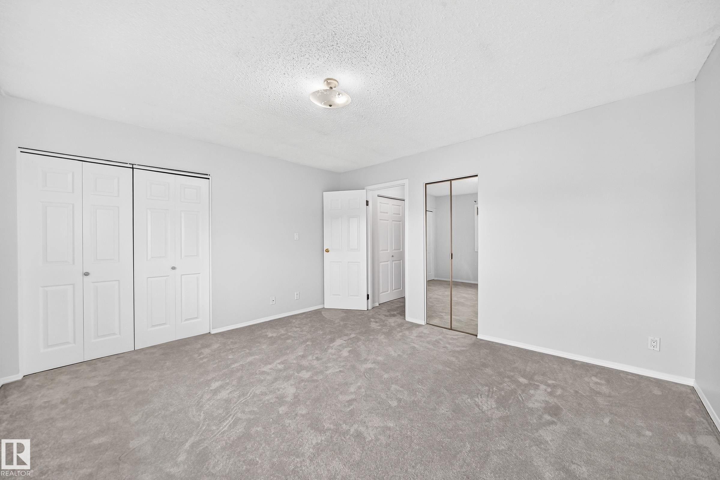 Spacious room featuring light gray carpeting, neutral wall paint, a white bi-fold closet, and a mirrored closet - 11447 22 Avenue Nw, Edmonton, AB - Indoor Photo Showing Other Room