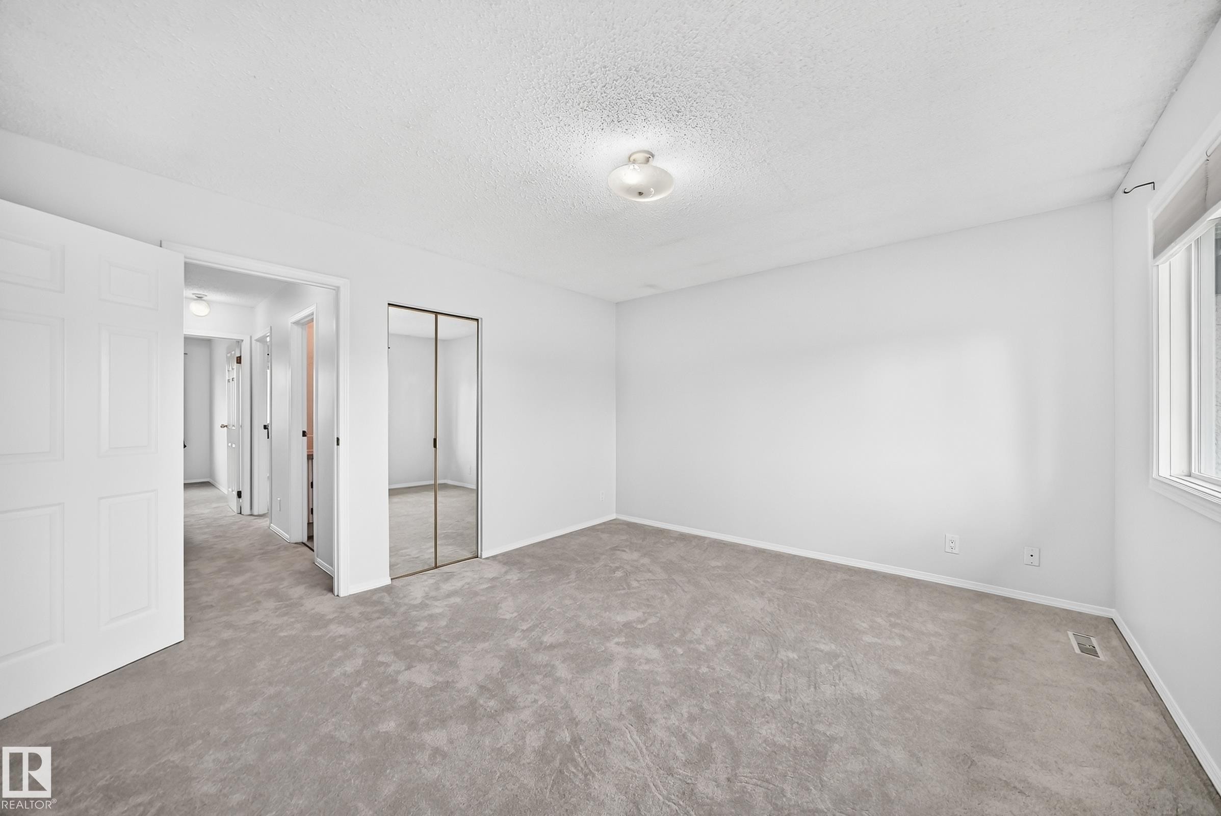 Room featuring neutral carpeting, white walls, a large window, a ceiling light fixture, and mirrored closet doors - 11447 22 Avenue Nw, Edmonton, AB - Indoor Photo Showing Other Room