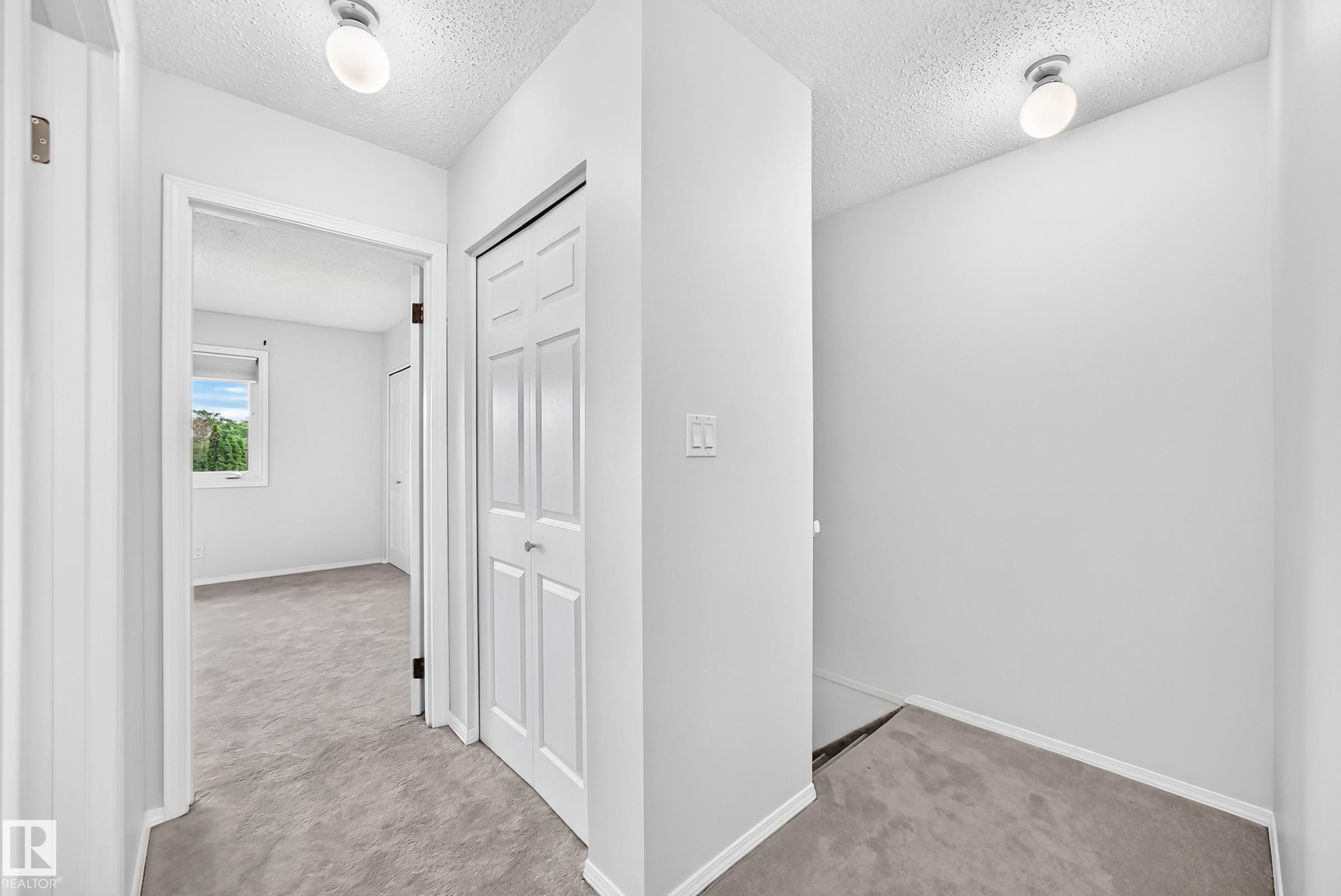 Hallway featuring light gray carpeting, white walls, and a paneled bifold closet door - 11447 22 Avenue Nw, Edmonton, AB - Indoor Photo Showing Other Room