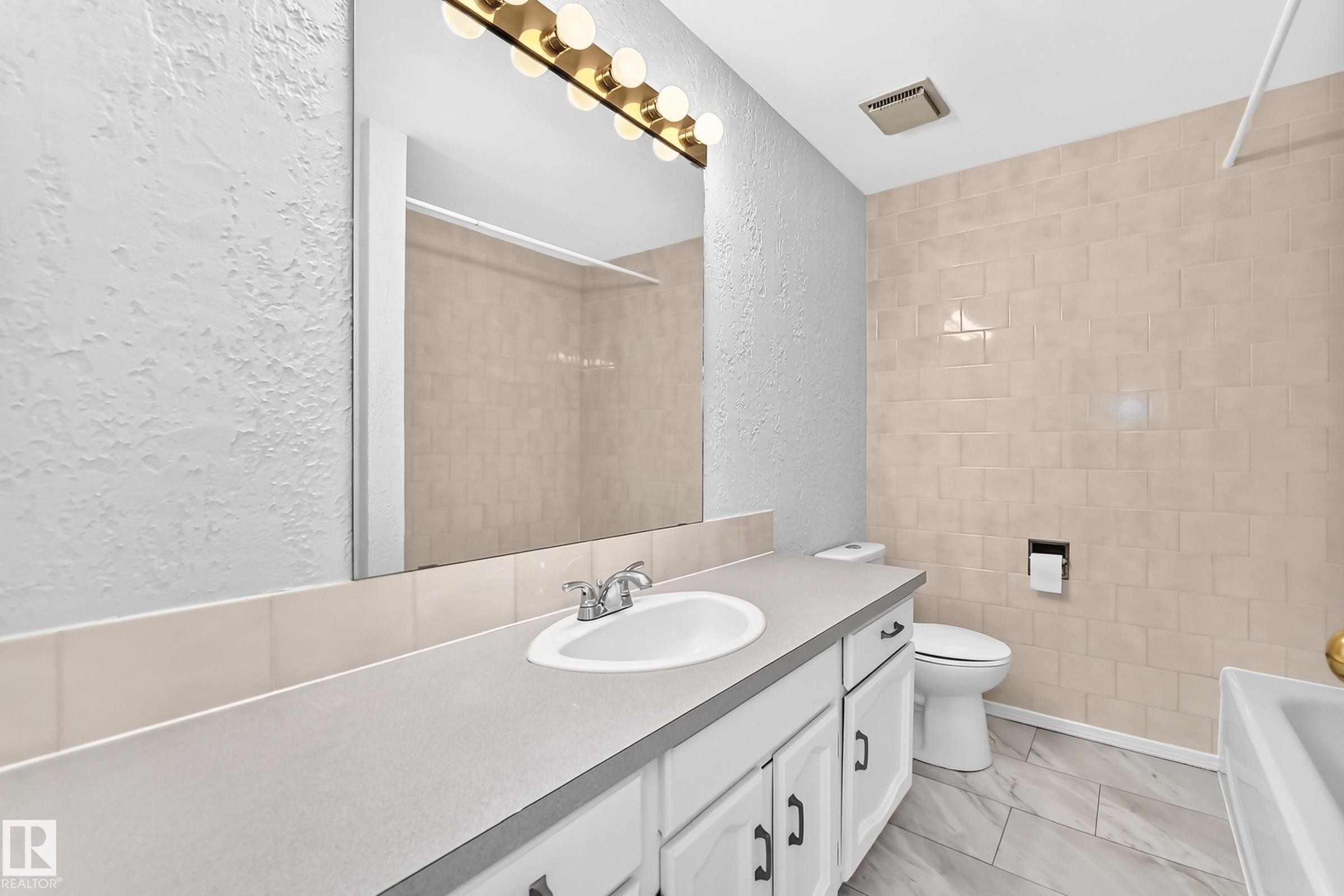 Bathroom featuring a vanity with a white integrated sink, chrome faucet, and white cabinetry with dark hardware - 11447 22 Avenue Nw, Edmonton, AB - Indoor Photo Showing Bathroom