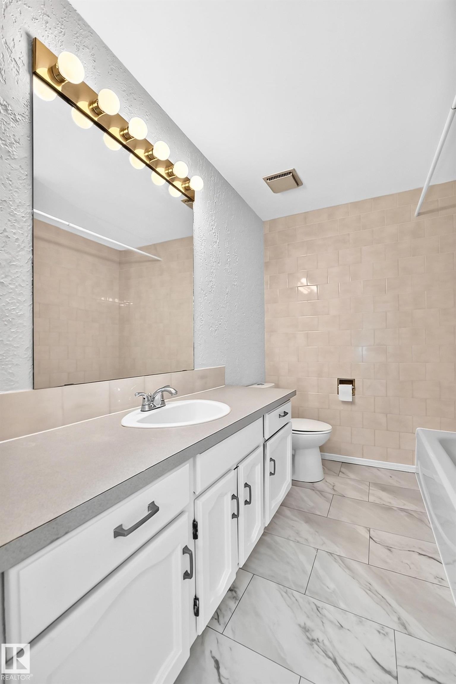 Bathroom featuring a vanity with an integrated sink, broad mirror, and a wall-mounted light bar - 11447 22 Avenue Nw, Edmonton, AB - Indoor Photo Showing Bathroom