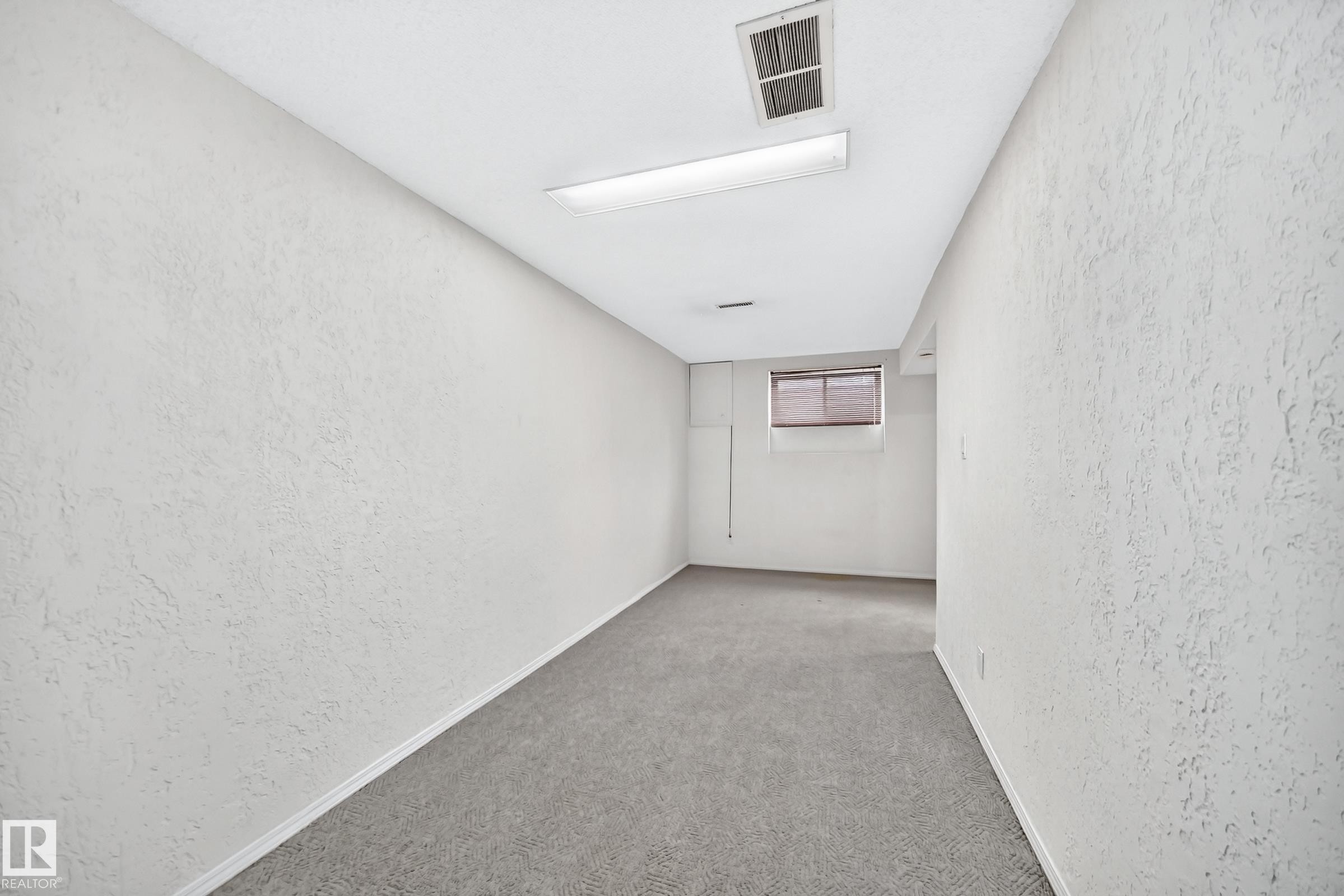 Spacious room featuring textured white walls, gray carpet, a single window with blinds, a white ceiling, and fluorescent lighting - 11447 22 Avenue Nw, Edmonton, AB - Indoor Photo Showing Other Room