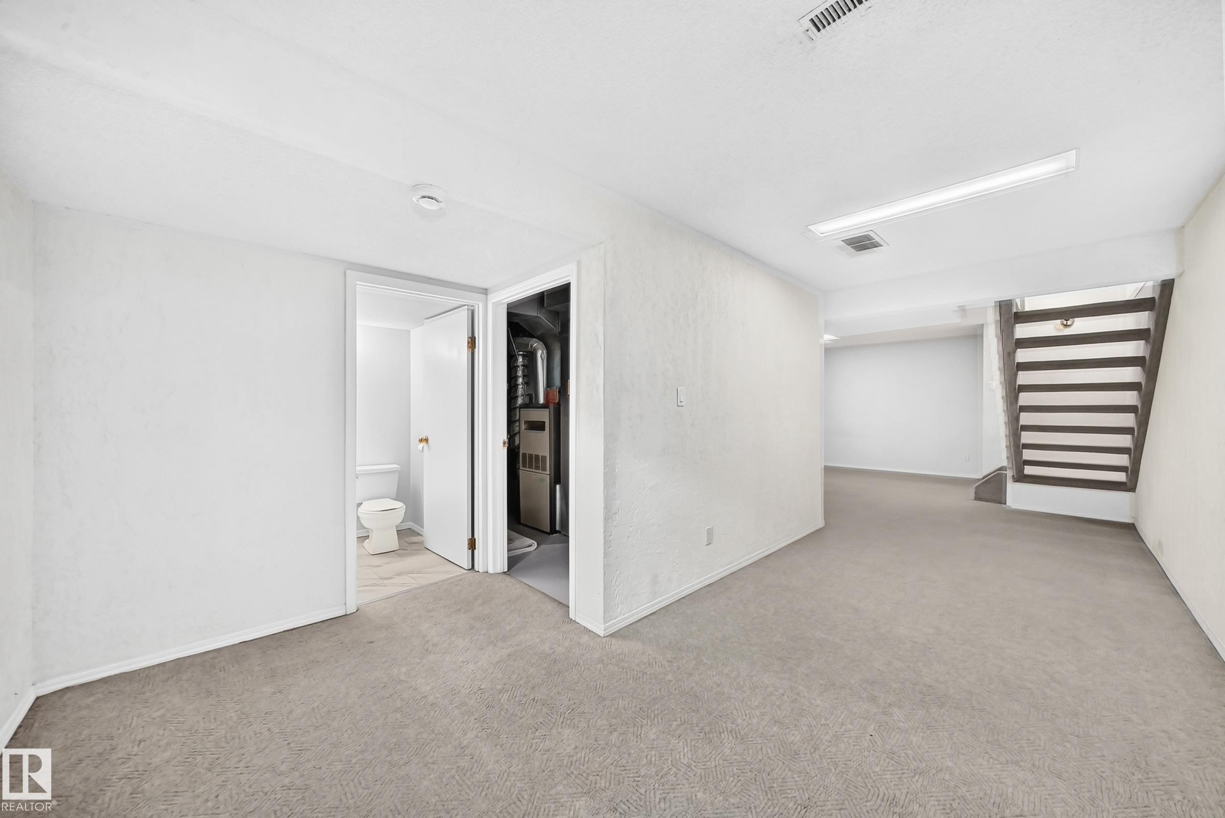 Carpeted lower level featuring a light neutral color palette, recessed lighting, and a partially visible bathroom with a toilet - 11447 22 Avenue Nw, Edmonton, AB - Indoor Photo Showing Other Room