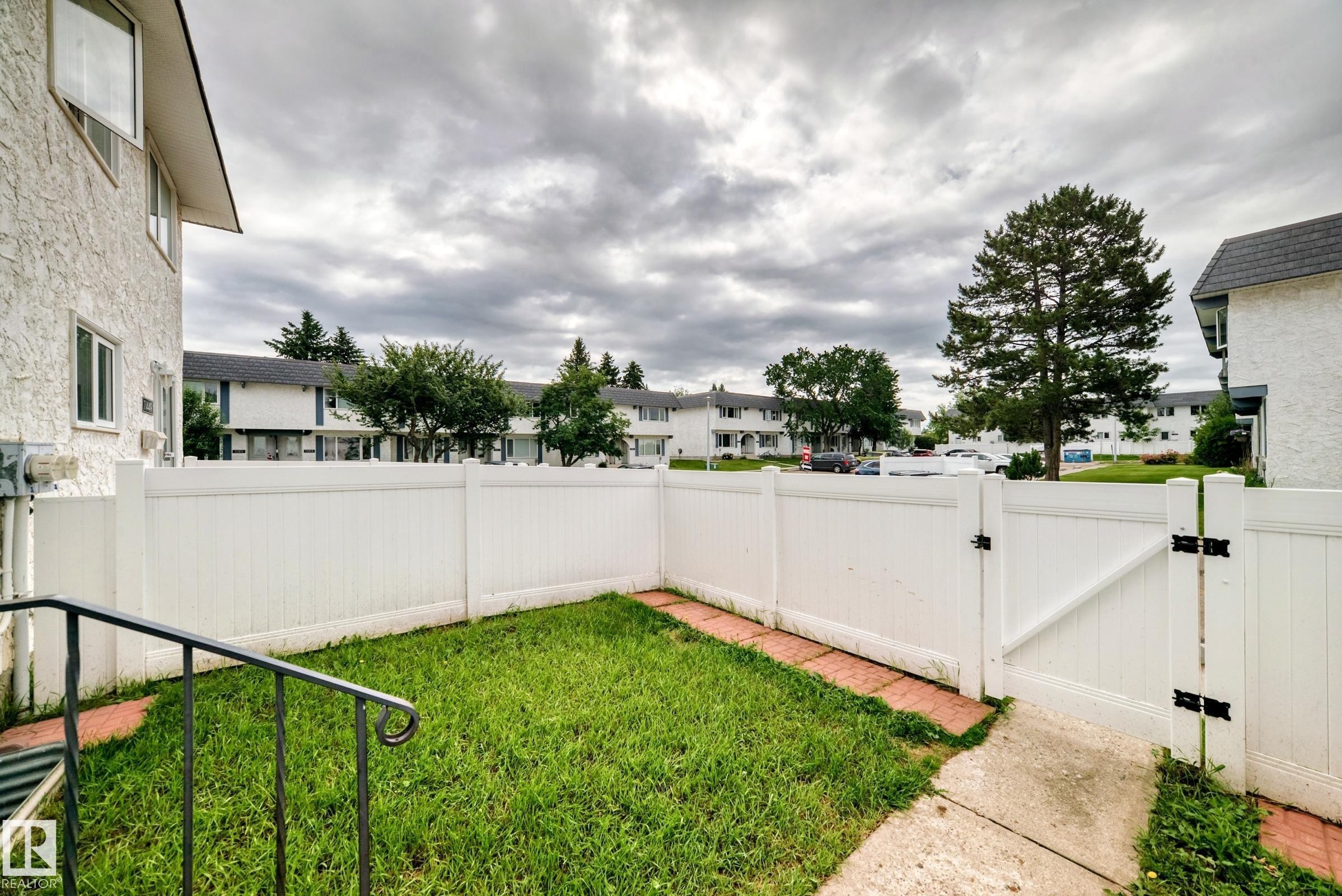 Fenced outdoor area featuring a white privacy fence with gate, concrete pathway, and a small lawn - 11447 22 Avenue Nw, Edmonton, AB - Outdoor