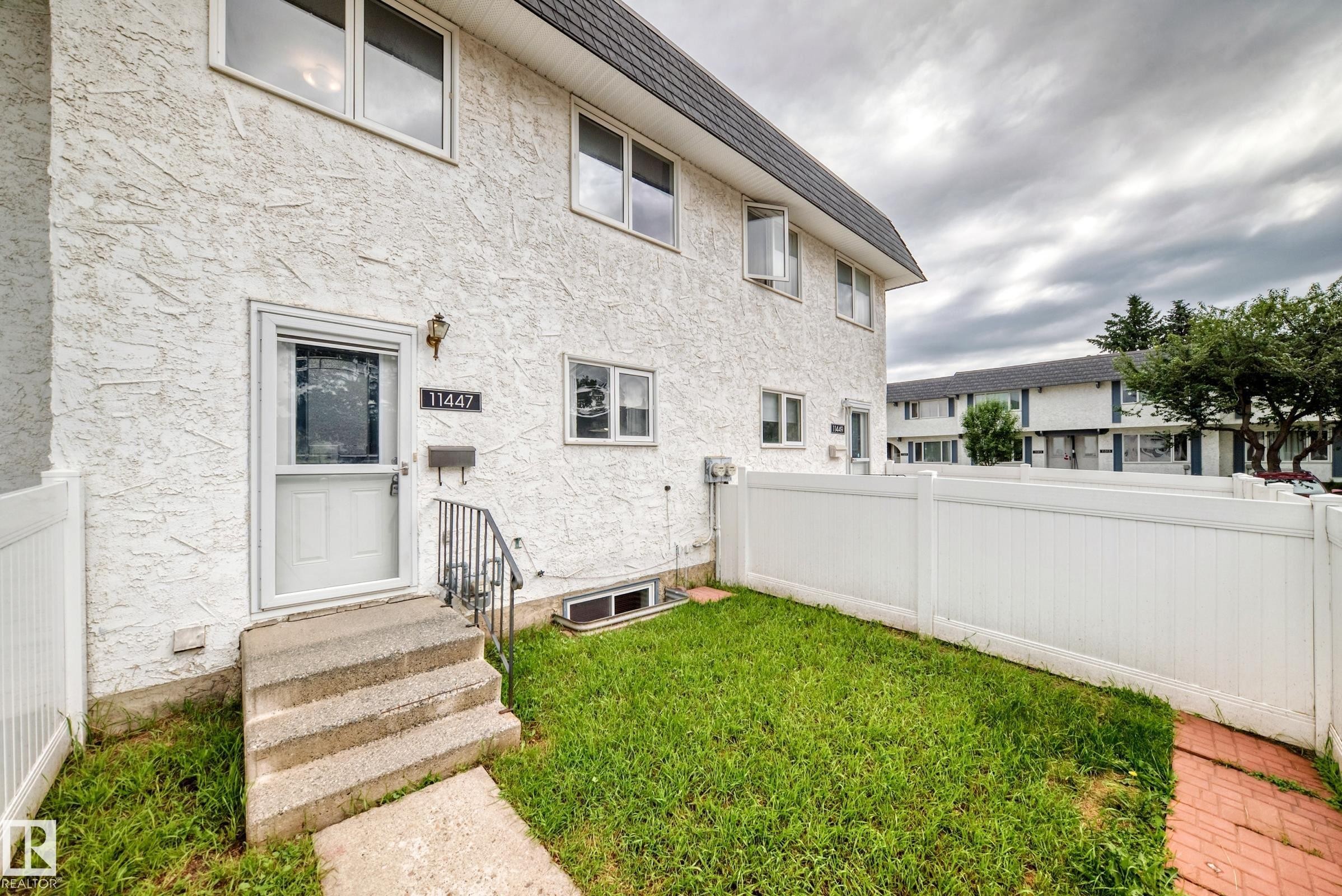 Stucco exterior with multiple windows, a concrete staircase, and a white screen door - 11447 22 Avenue Nw, Edmonton, AB - Outdoor