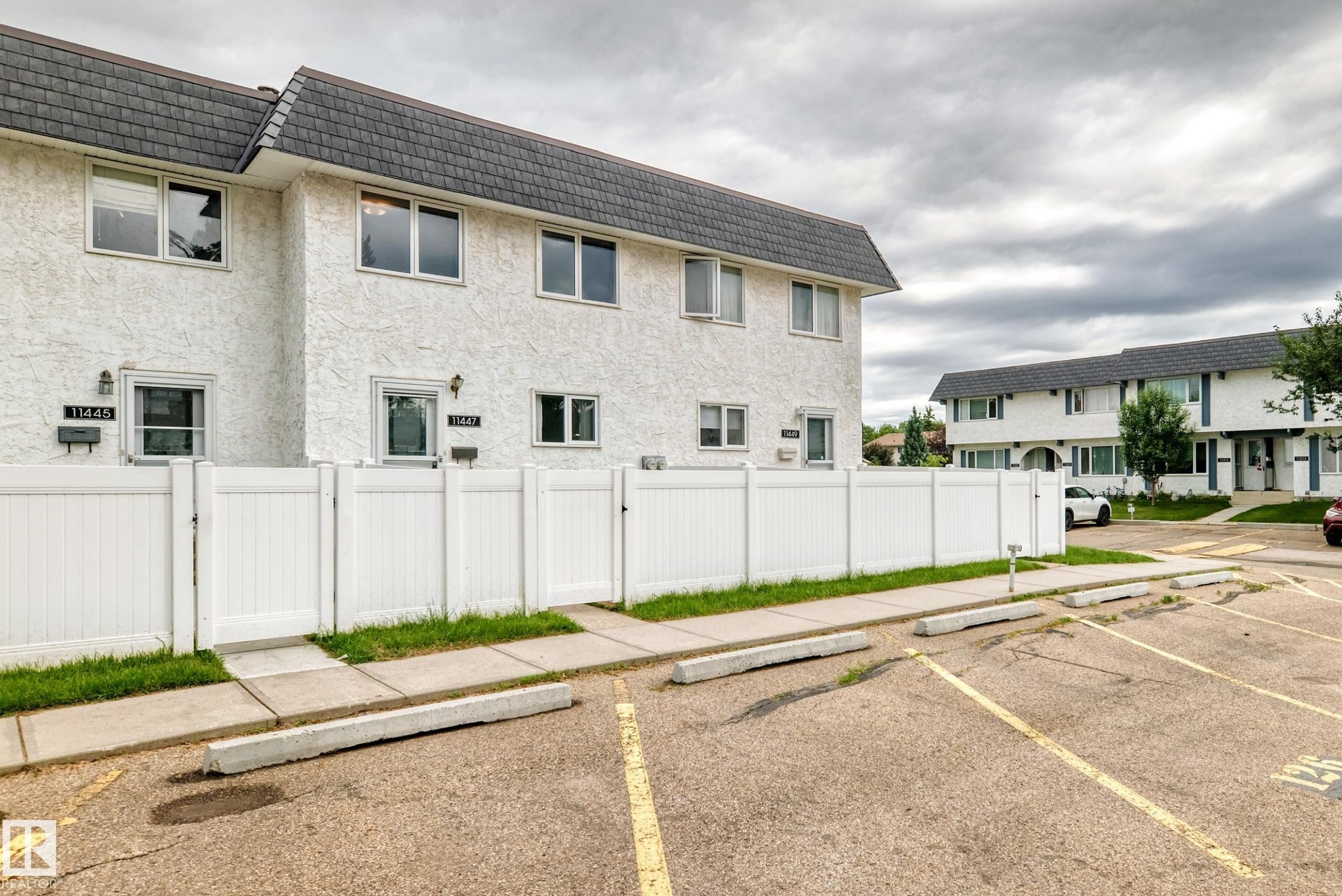 Multi-unit residential building featuring a textured white exterior, contrasting dark shingle roof, and white-framed windows - 11447 22 Avenue Nw, Edmonton, AB - Outdoor