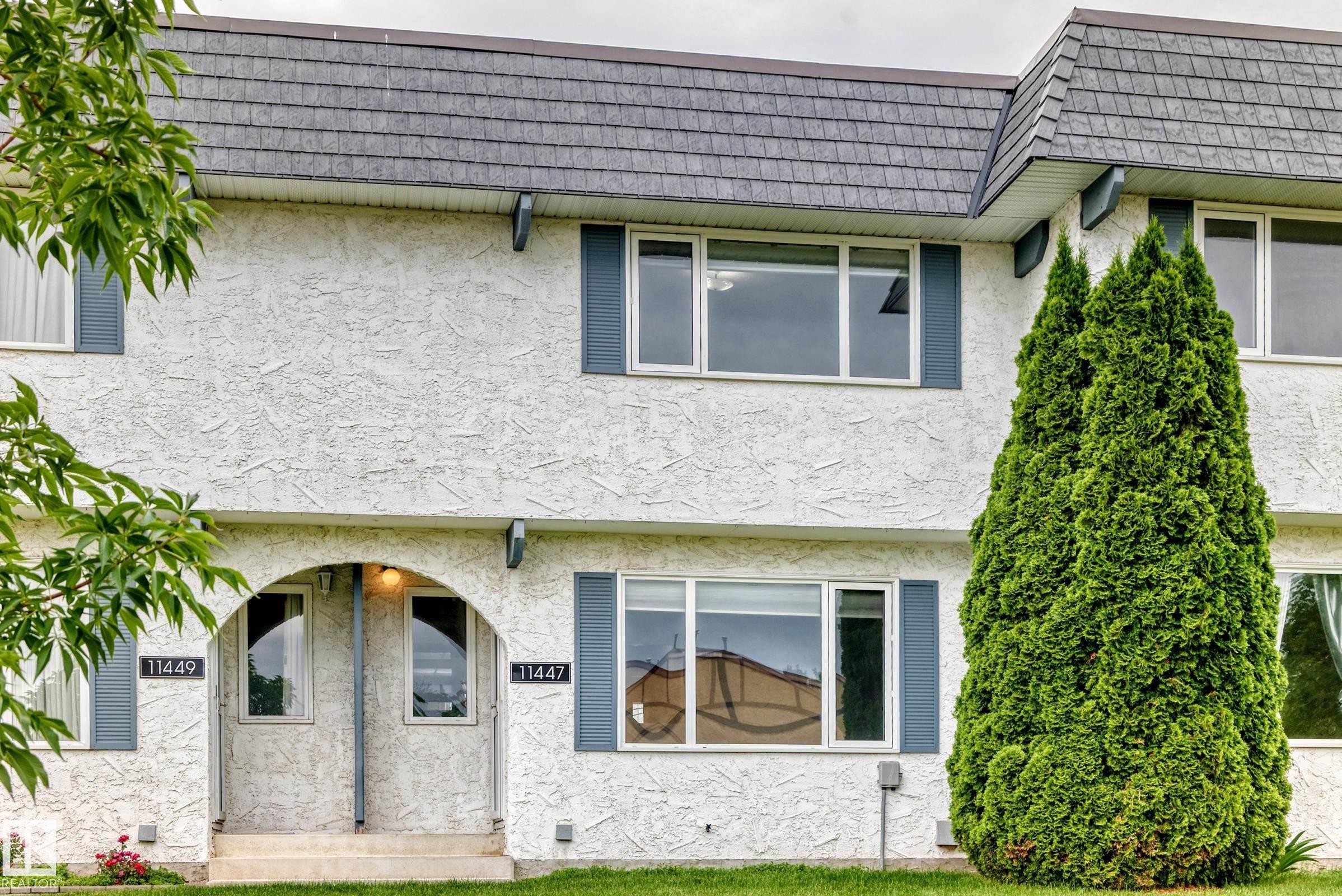 Multi-level residence featuring textured white stucco exterior, grey shingle roofing, and blue decorative shutters - 11447 22 Avenue Nw, Edmonton, AB - Outdoor