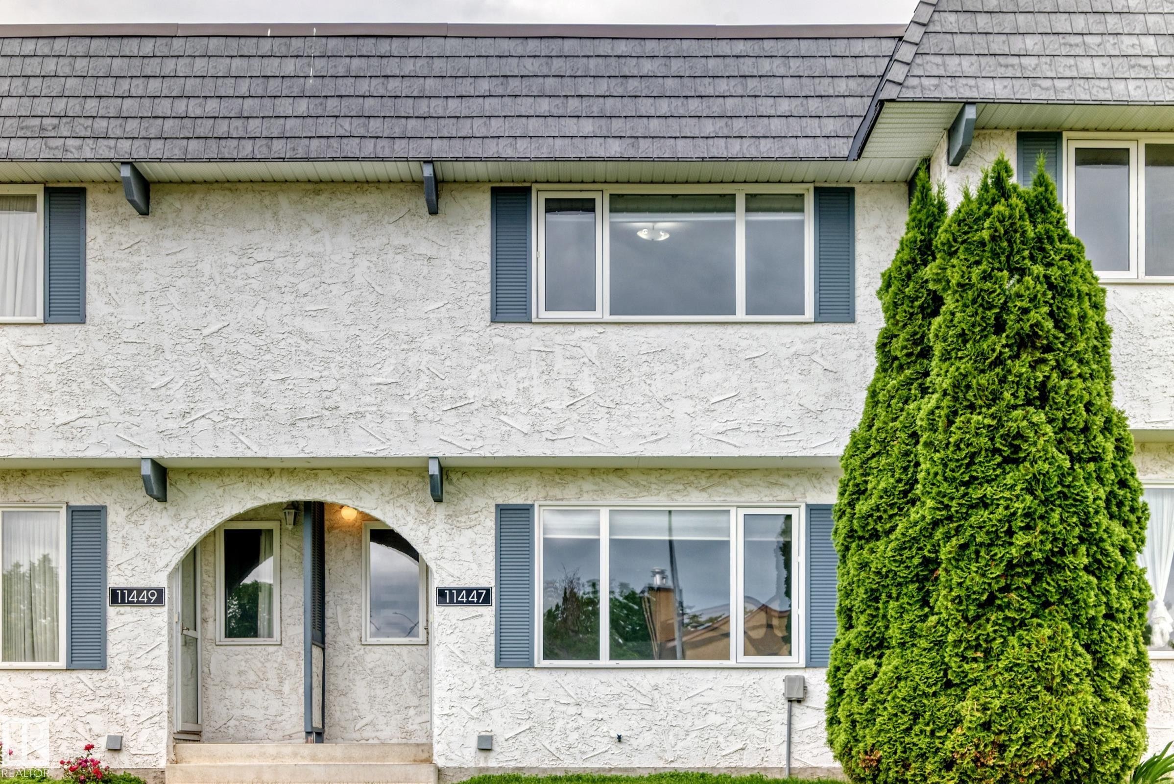 Stucco exterior featuring an arched entryway, shingle roof, and multiple windows with dark shutters - 11447 22 Avenue Nw, Edmonton, AB - Outdoor With Exterior