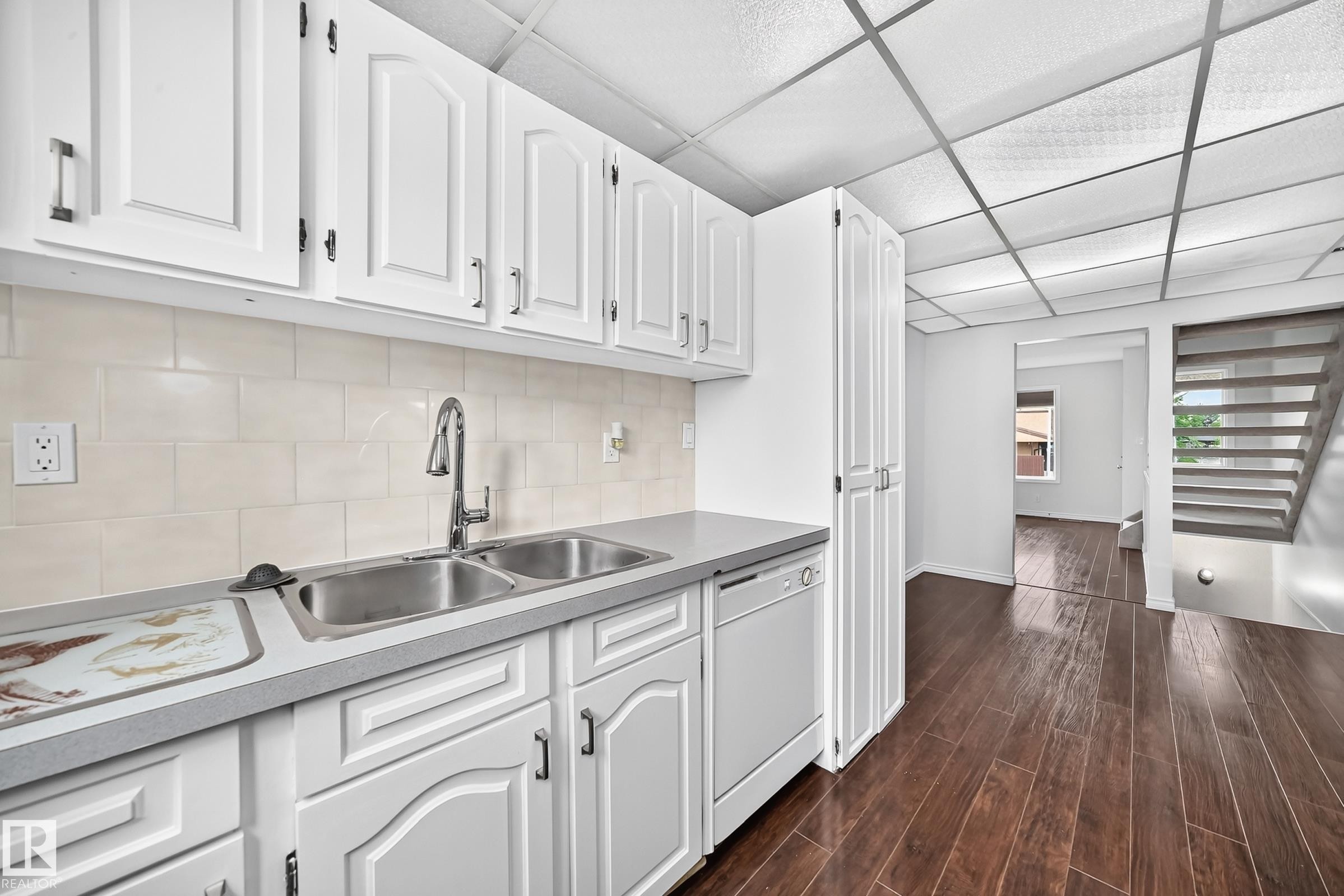 Kitchen featuring white cabinetry, a double basin stainless steel sink, and light-colored tile backsplash - 11447 22 Avenue Nw, Edmonton, AB - Indoor Photo Showing Kitchen With Double Sink