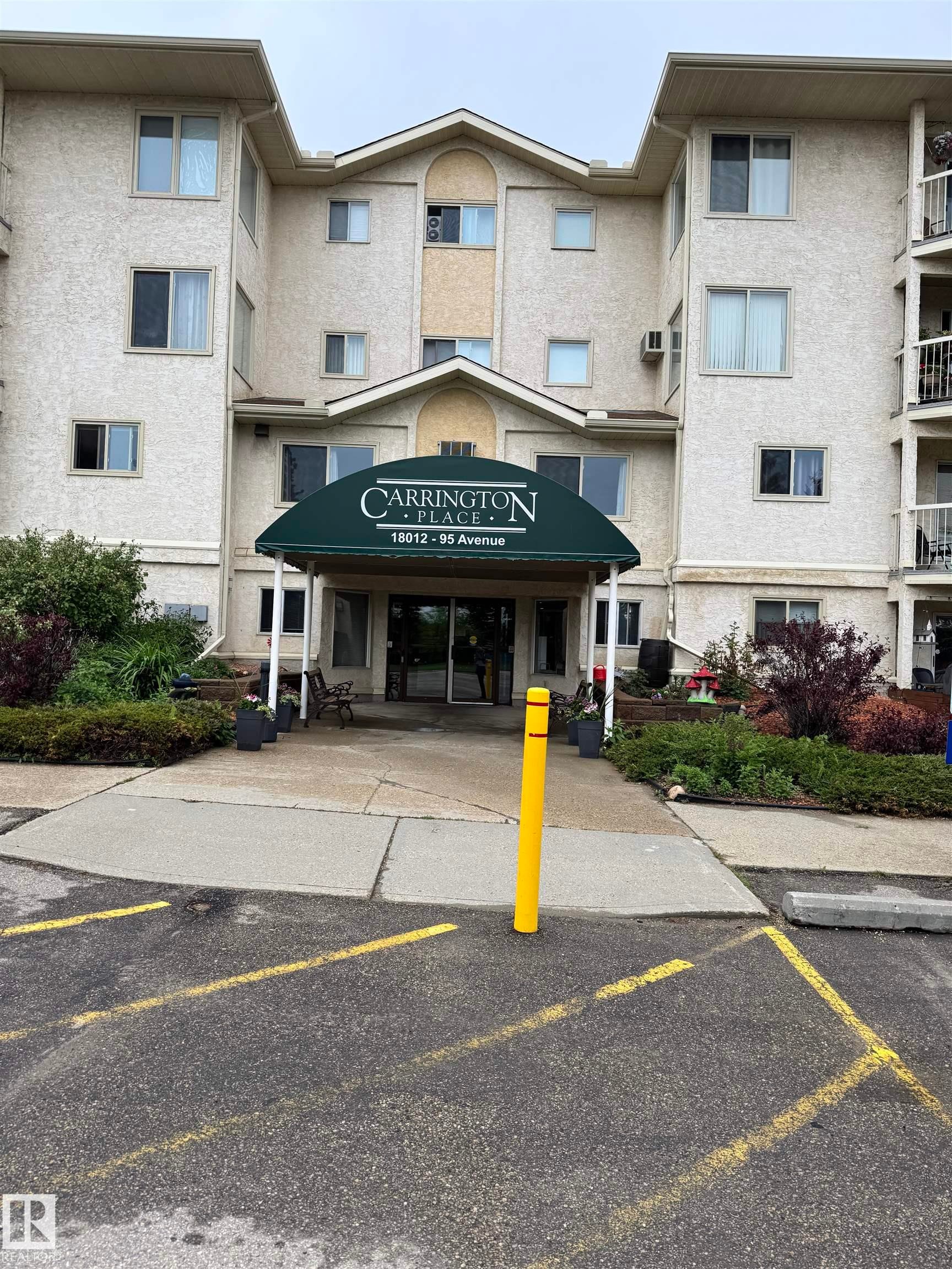 Multi-story stucco exterior building featuring a prominent entrance canopy, well-maintained landscaping, and visible balconies - 207 18012 95 Avenue, Edmonton, AB