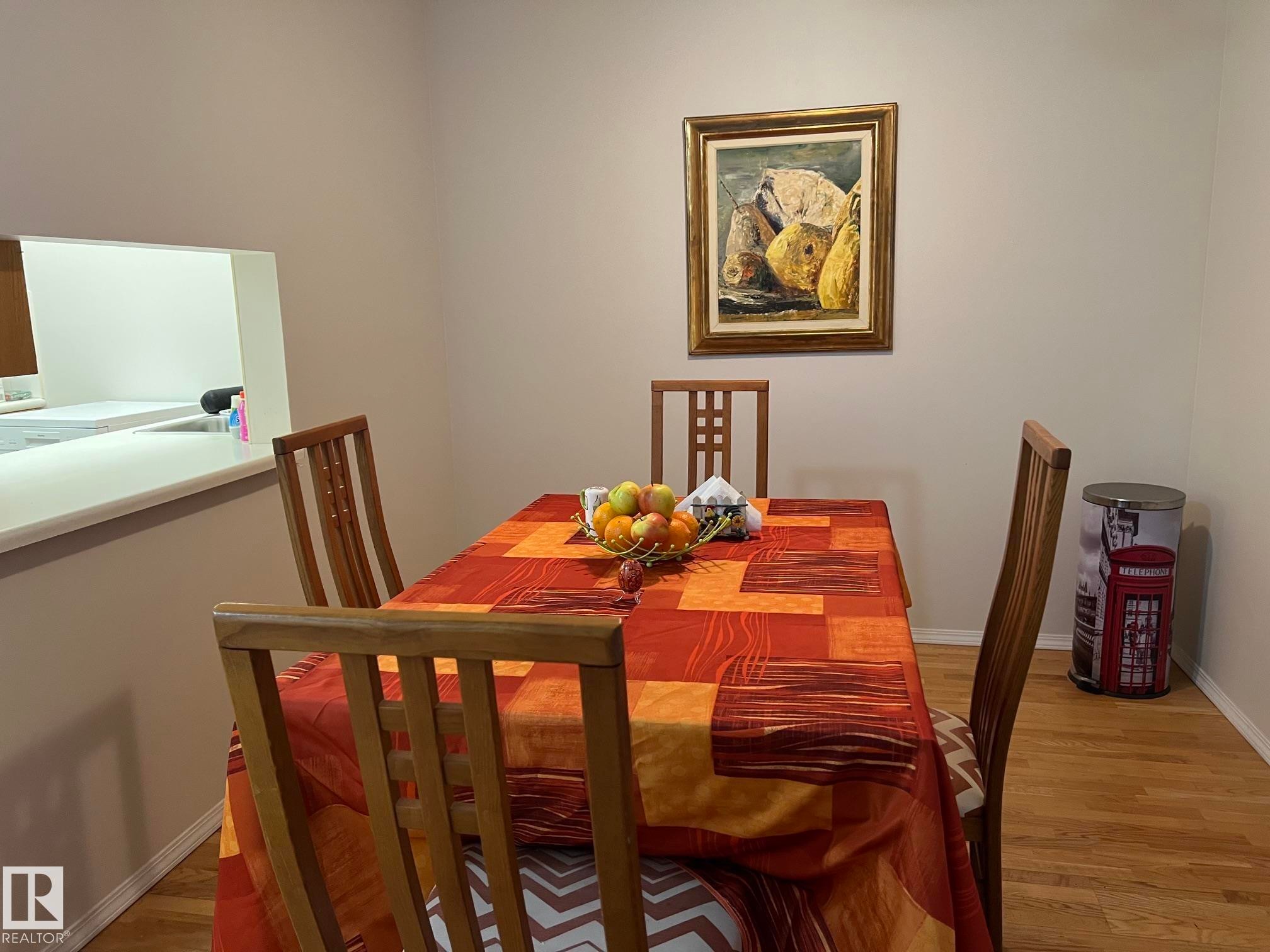 Dining area featuring wood-finish flooring and a pass-through window with white countertop - 207 18012 95 Avenue, Edmonton, AB