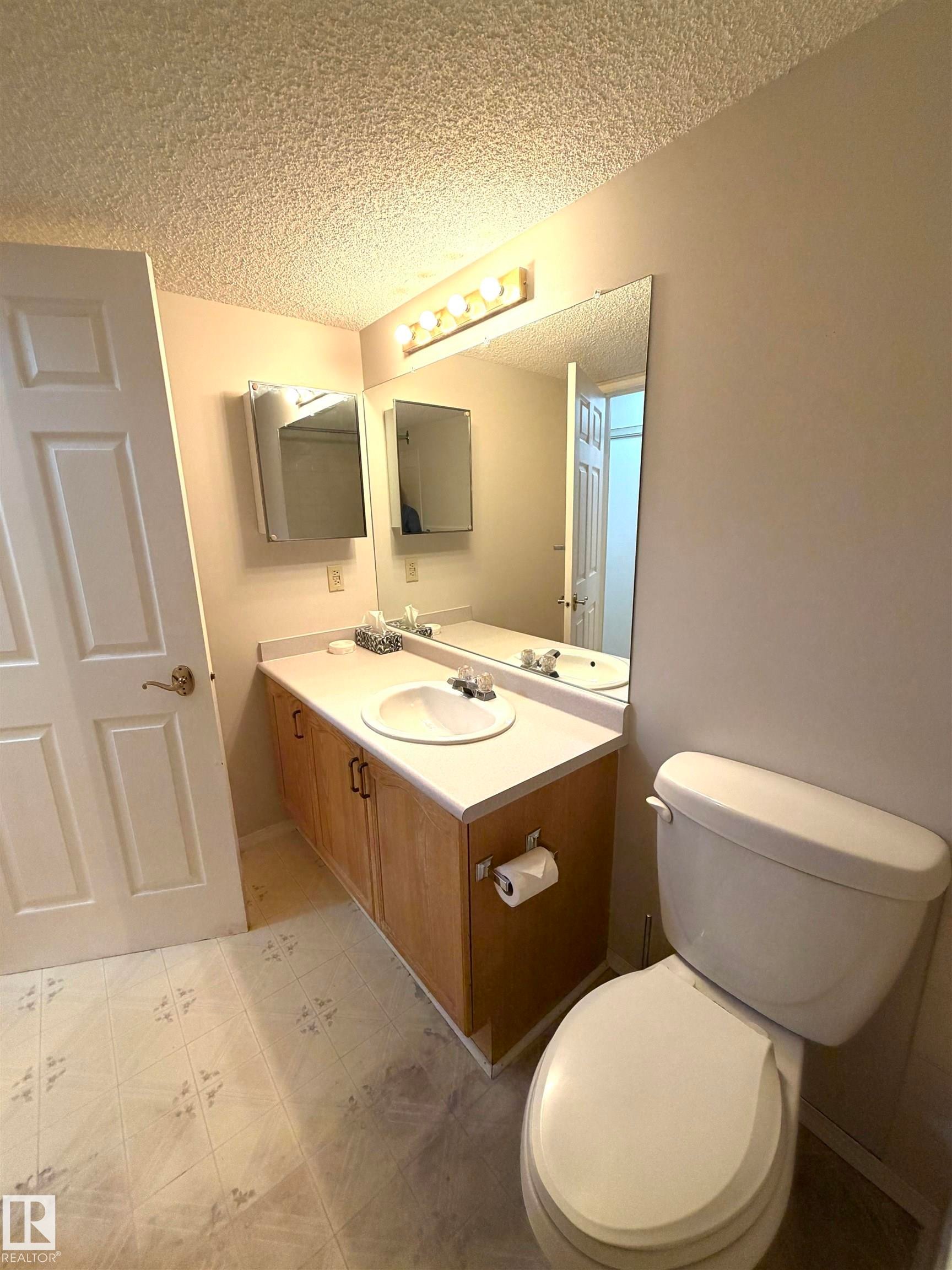 Bathroom featuring a single vanity with wood-finish cabinetry, a white countertop, and an integrated sink with a chrome faucet - 207 18012 95 Avenue, Edmonton, AB