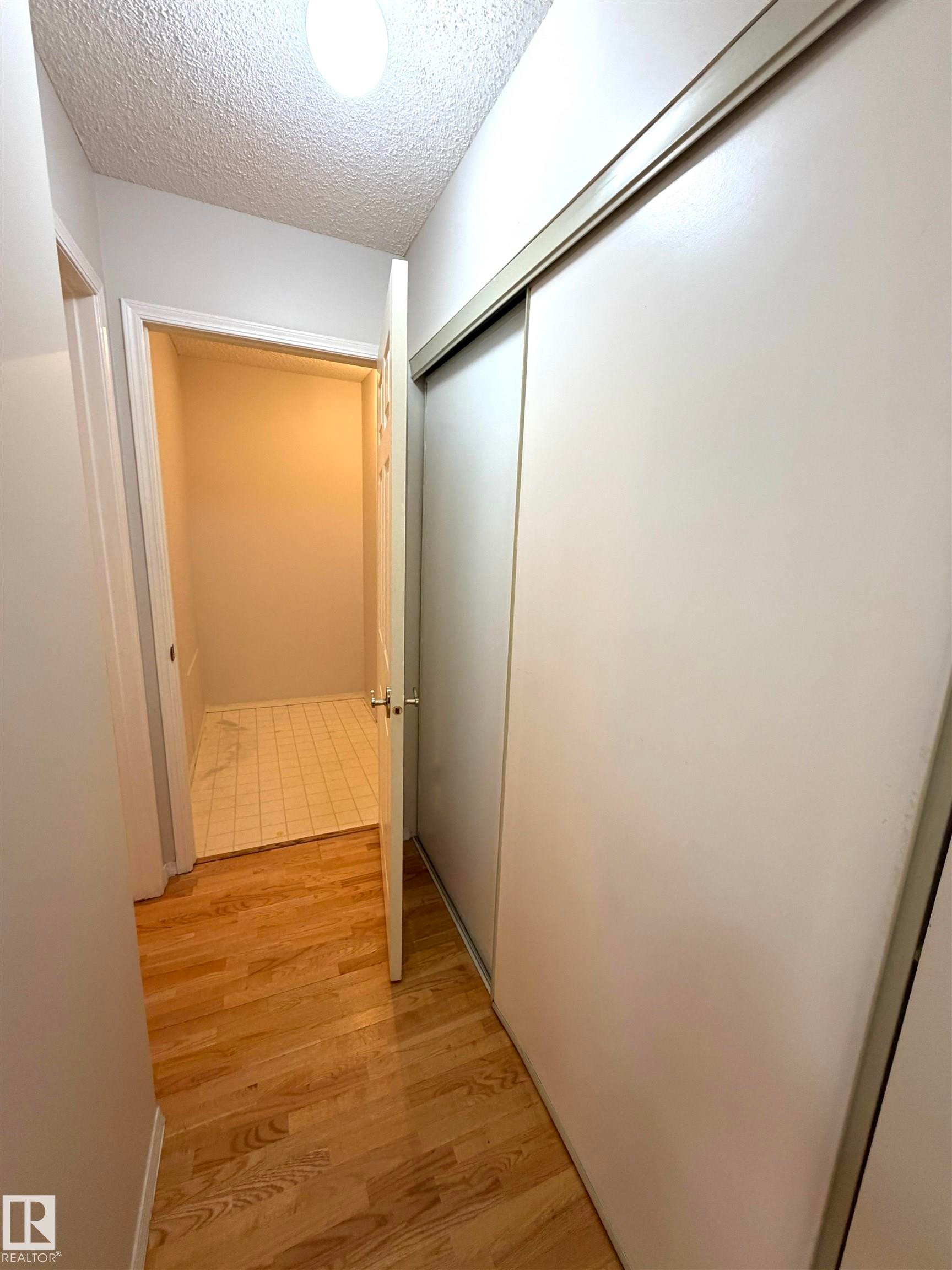 Hallway featuring wood-finish flooring and a white sliding closet door - 207 18012 95 Avenue, Edmonton, AB
