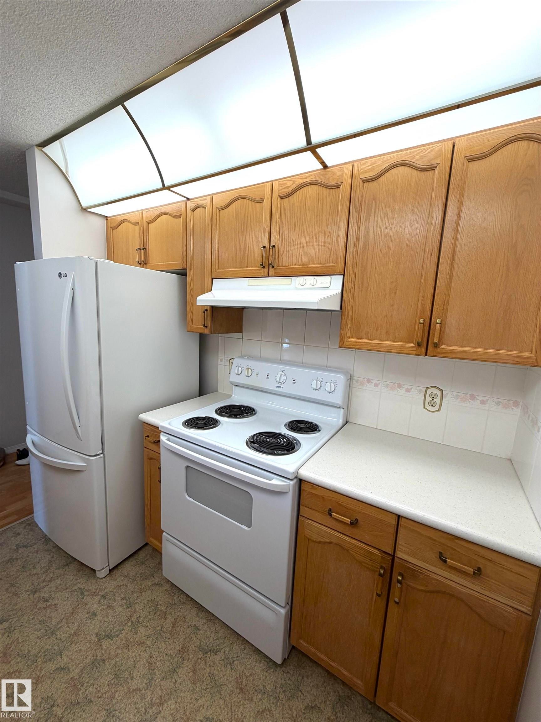 Kitchen featuring wood-finish cabinetry, white countertops, and white appliances - 207 18012 95 Avenue, Edmonton, AB