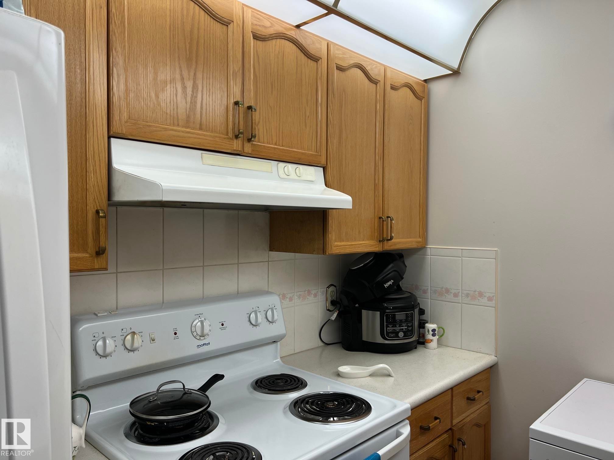 Kitchen area with wood-finish cabinetry and a white range hood - 207 18012 95 Avenue, Edmonton, AB