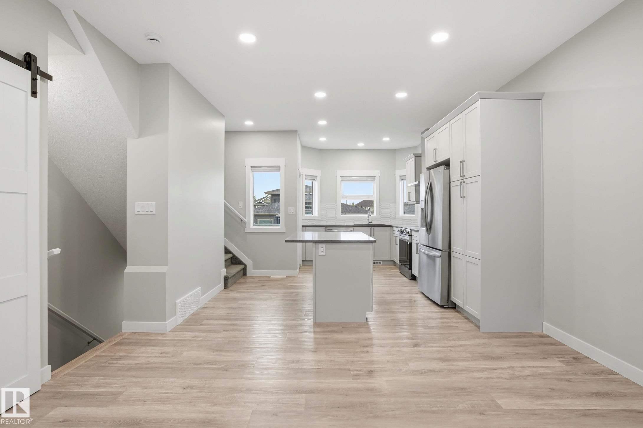 Open-concept kitchen and living area featuring wood-finish flooring, white shaker cabinetry, stainless steel appliances, a center island with countertop seating, and recessed lighting - 36 150 Everitt Dr, St. Albert, AB - Indoor Photo Showing Kitchen